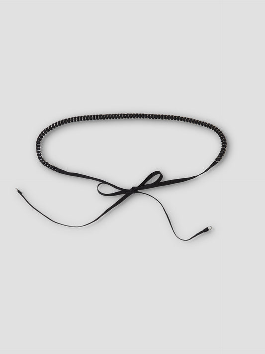 The Ring Loop Belt - Black features a coiled, choker-inspired design with thin ribbon ties in a bow, metallic tip detail, and adjustable wrap styling for a custom fit. Shown against a plain white background.