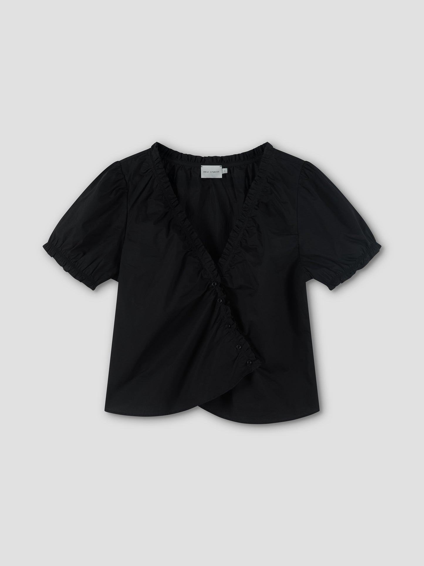 The Cross Frill Top is a black, short-sleeved blouse featuring a V-neckline, ruffled trim, and front buttons, shown against a light gray background.