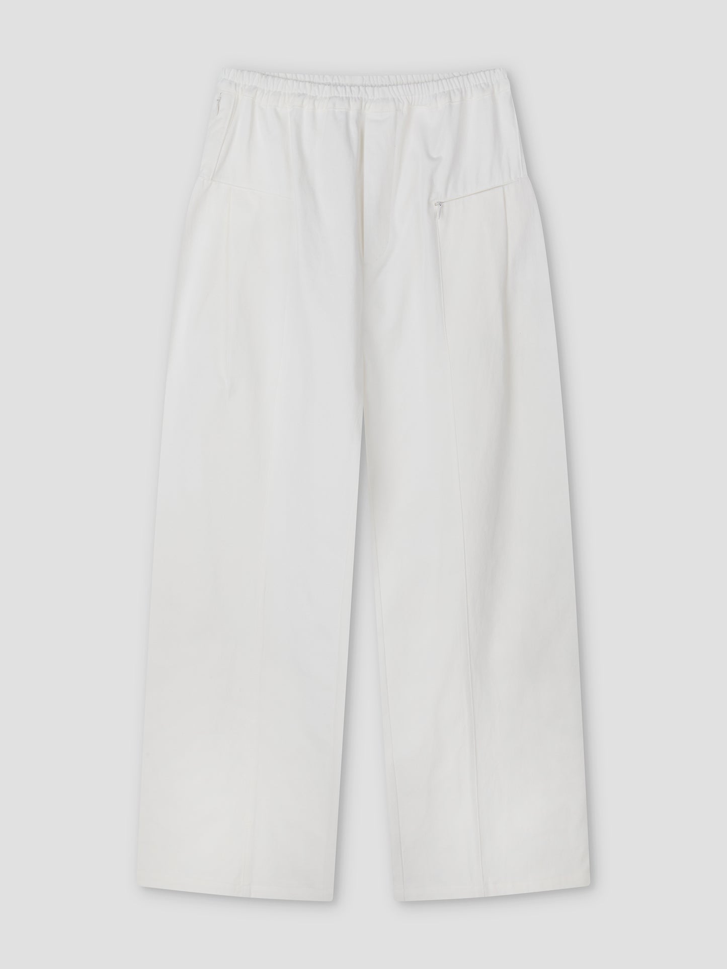 The Pleat Pant - White by Deiji Studios features an elastic waistband, side pockets, and a relaxed fit, shown laid flat on a light gray background.