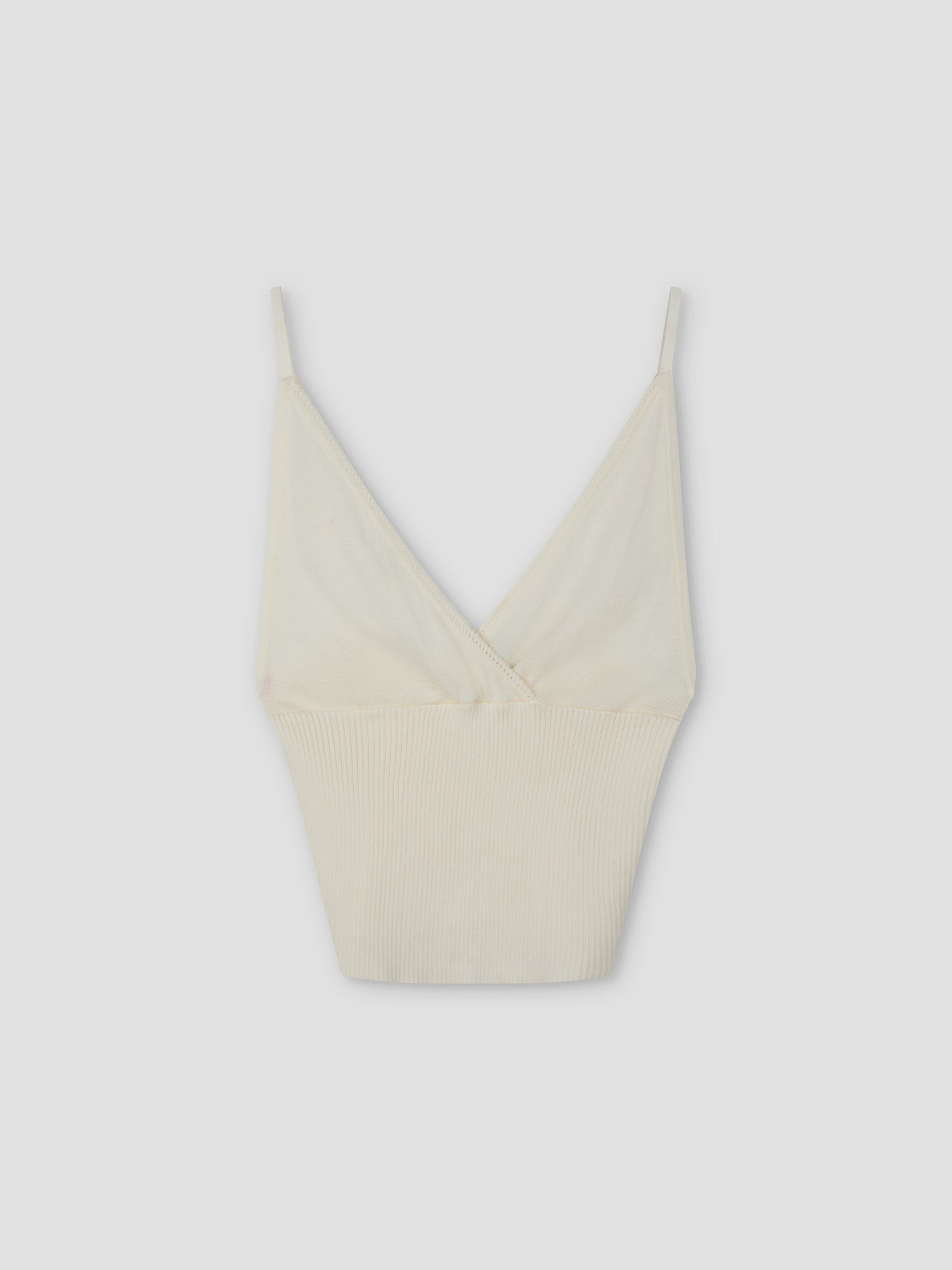The Cross Panel Knit Top - Off White features a cream hue, thin spaghetti straps, and a deep V neckline in a cross-panel knit style inspired by Deiji Studios, shown against a plain light gray background.
