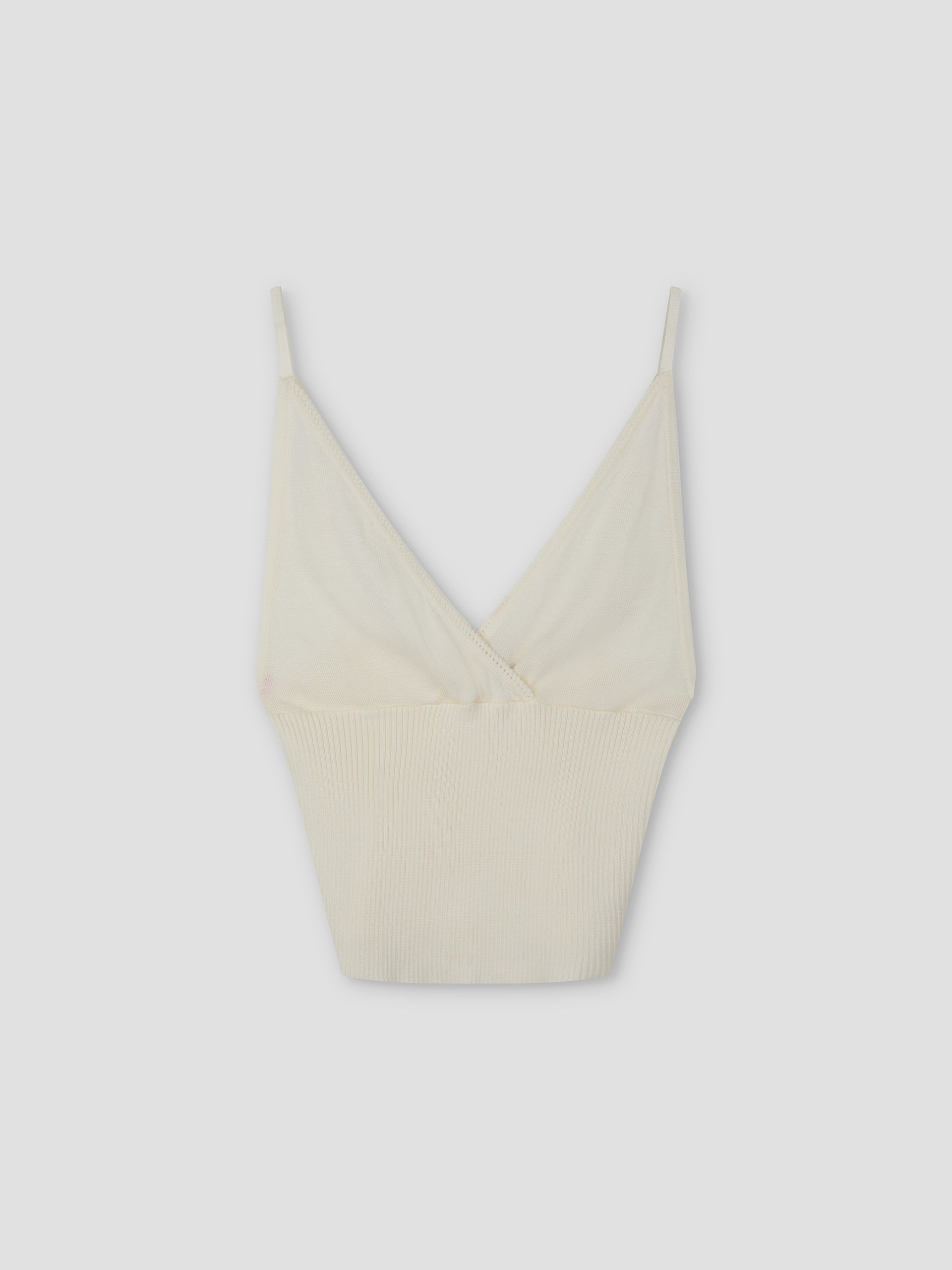 The Cross Panel Knit Top - Off White features a cream hue, thin spaghetti straps, and a deep V neckline in a cross-panel knit style inspired by Deiji Studios, shown against a plain light gray background.