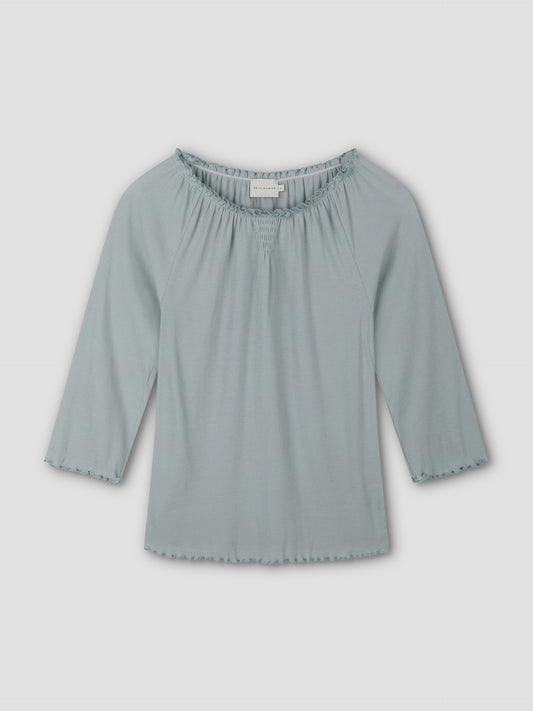 The Cotton Flounce 3/4 Sleeve - Baby Blue by Deiji Studios is a women’s top with a gathered, elastic neckline and softly ruffled edges on the sleeves and hem, shown laid flat on a plain white background.