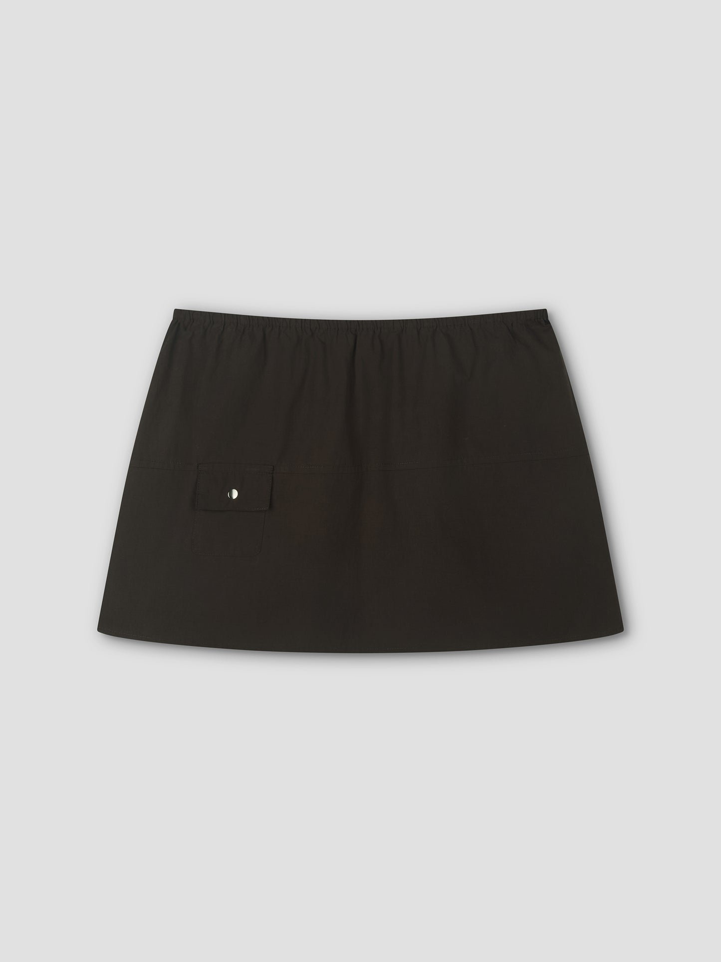 The Pocket Skirt - Black by Deiji Studios is a mini-length skirt with an elastic waistband and a front left flap pocket with button, shown on a plain light gray background.