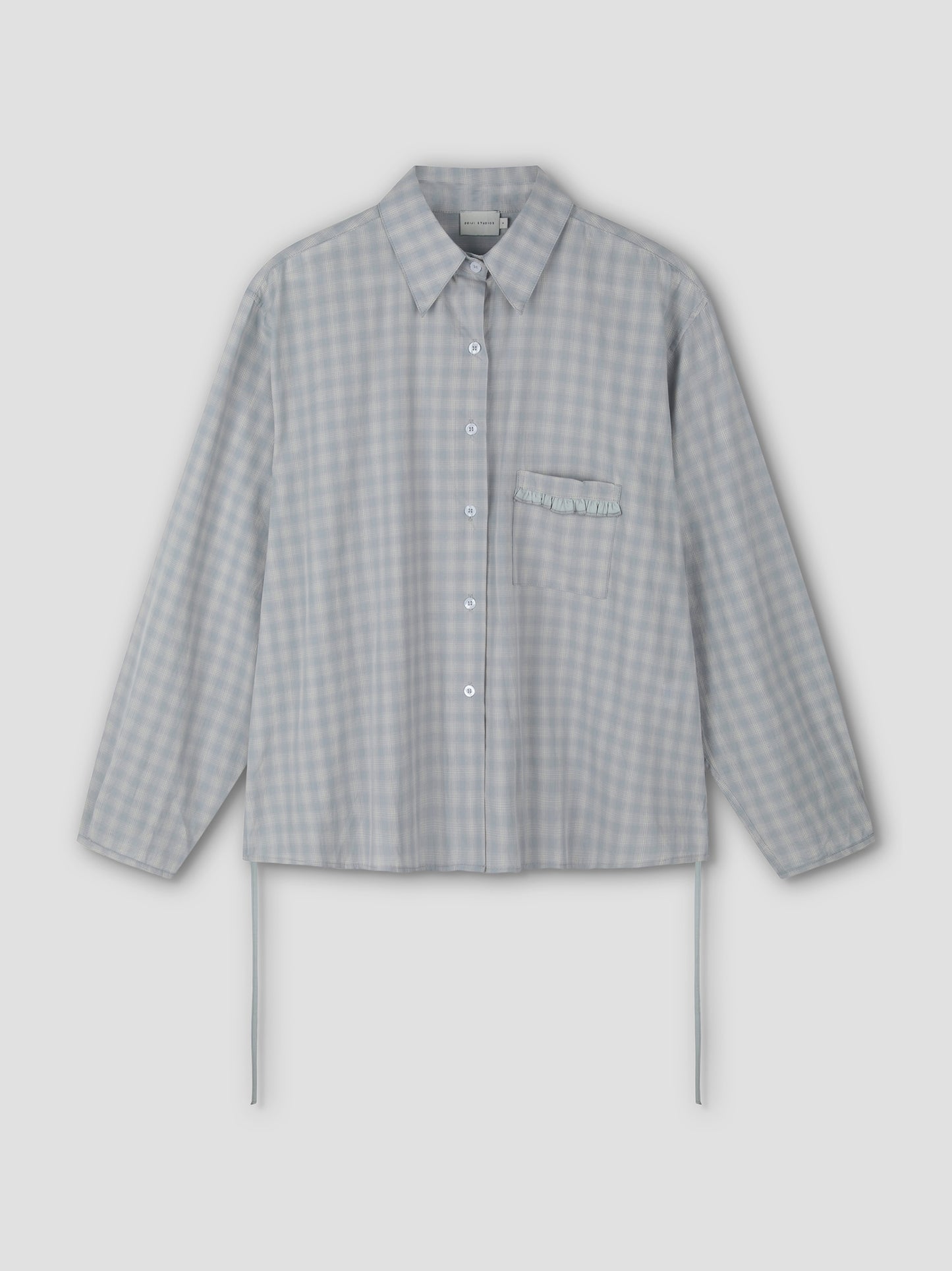 The Day Shirt - Blue Check features a light blue and white gingham pattern, boxy fit, long sleeves, collar, chest pocket with ruffle detail, and side ties. Shown as a button-up shirt on a plain light background.