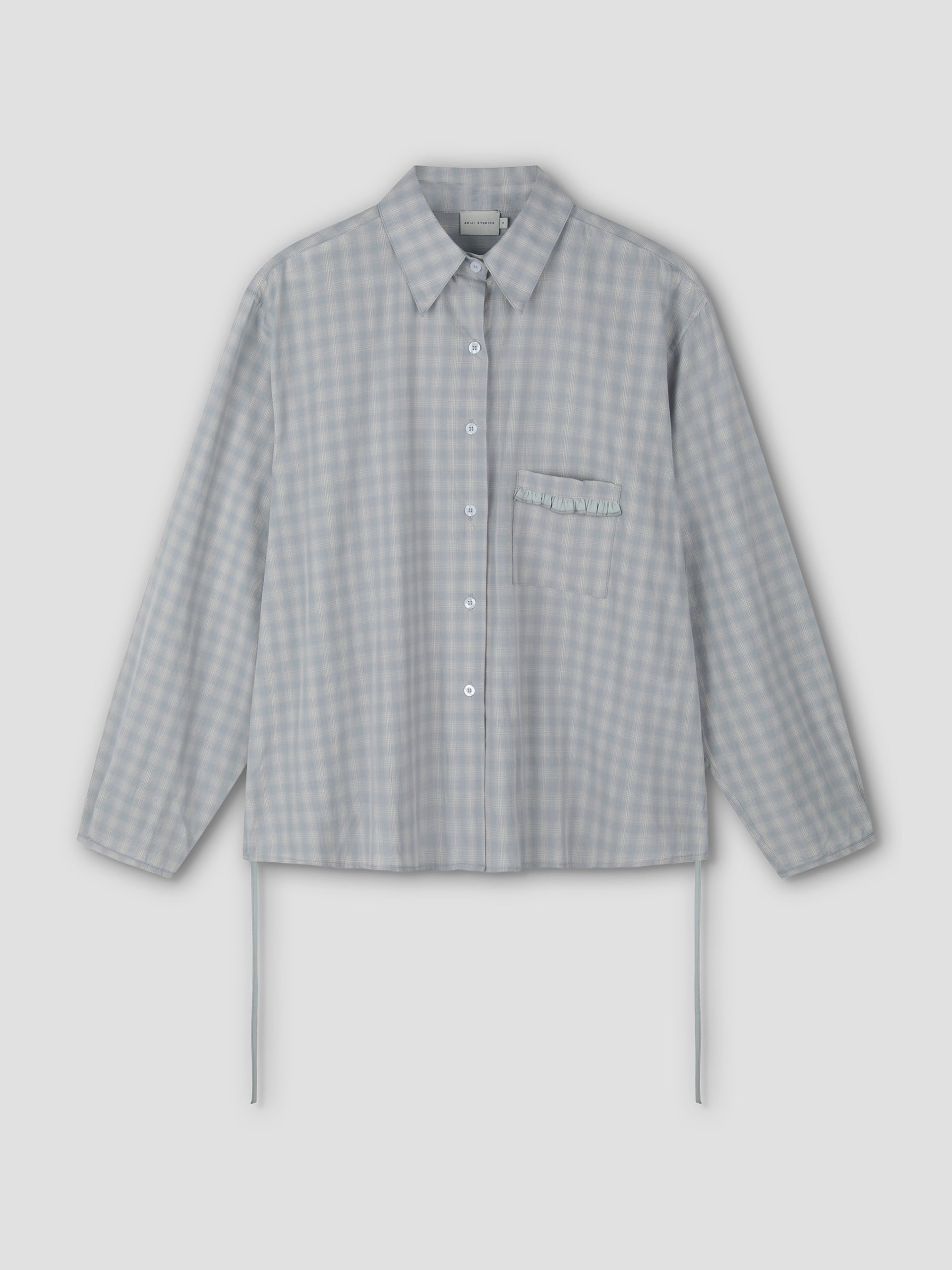 The Day Shirt - Blue Check features a light blue and white gingham pattern, boxy fit, long sleeves, collar, chest pocket with ruffle detail, and side ties. Shown as a button-up shirt on a plain light background.