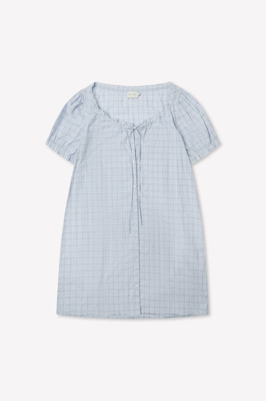 The Buttoned Mini Dress - Powder Check by Deiji Studios in light blue features a round neckline, front collar tie detail, and powder check pattern, shown laid flat on a white background.