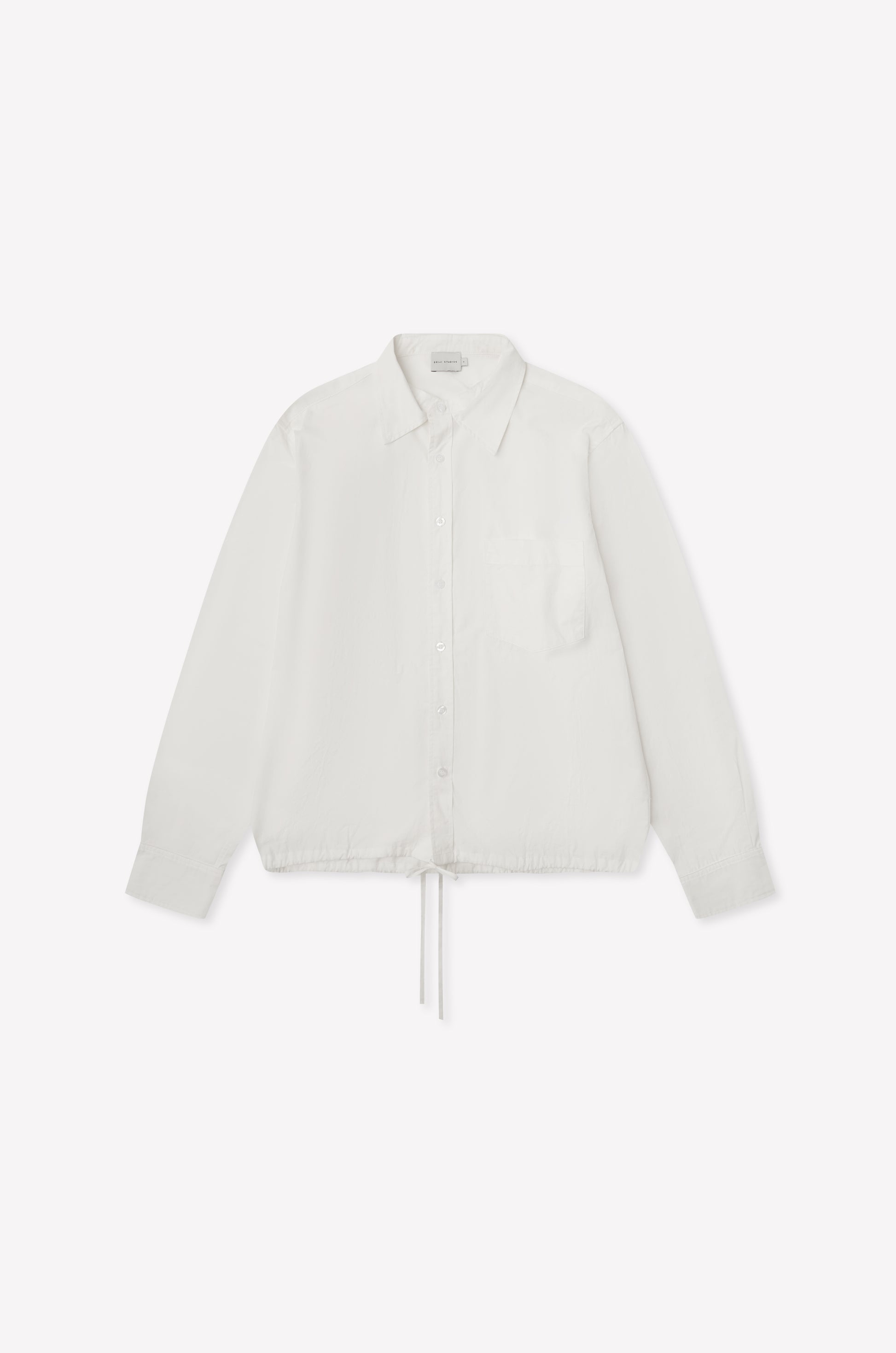 The Stand Shirt - White is a long-sleeved, oversized cotton shirt featuring a single chest pocket, mandarin collar, and drawstring hem, shown on a white background.