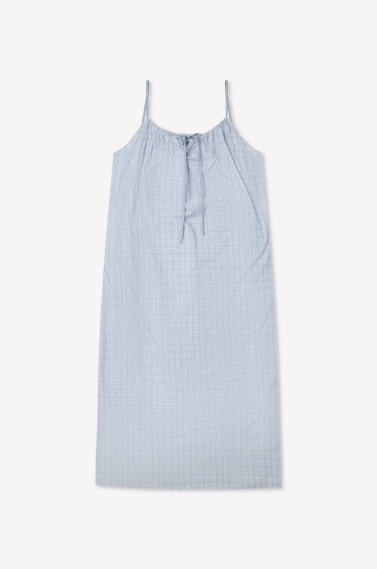 The Light Maxi Dress - Powder Check by Deiji Studios is a light blue sleeveless maxi made from organic cotton with thin straps, a gathered tie neckline, and a subtle check pattern, shown flat against a white background.