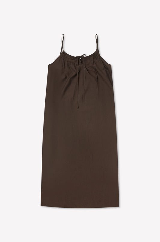 The Light Maxi Dress - Toast by Deiji Studios is a sleeveless, knee-length brown dress with thin straps and a gathered neckline tied with a bow, shown flat on a light background.