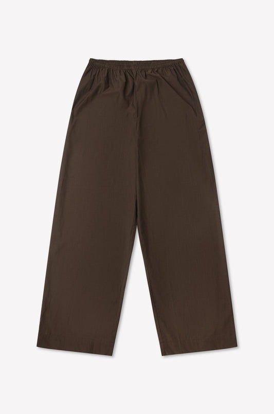 The Ease Trouser - Toast is a wide-leg brown pant with an elastic waistband, ankle length, and minimalist design. Laid flat on a plain white background, it features no visible pockets or extra details.