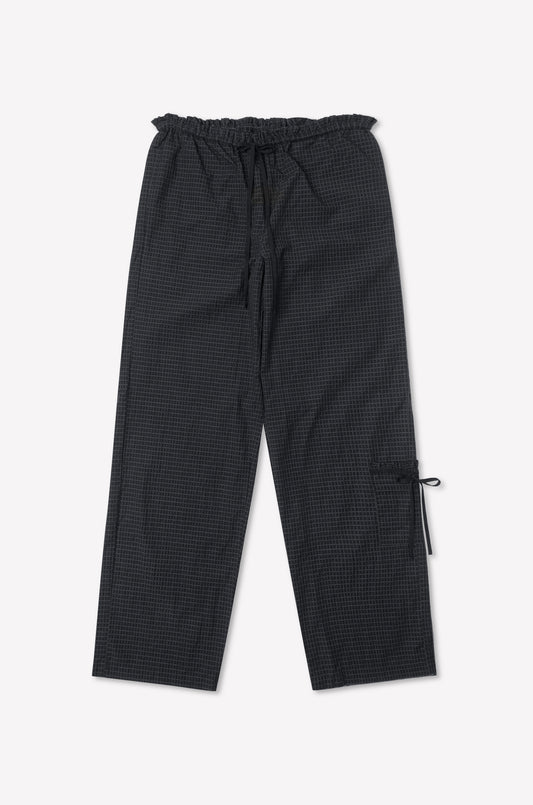 The Grosgrain Pant - Mono Grid is a loose-fit black checkered pant with relaxed legs, a drawstring waist, side pocket with tie detail, inspired by Deiji Studios, shown on a white background.