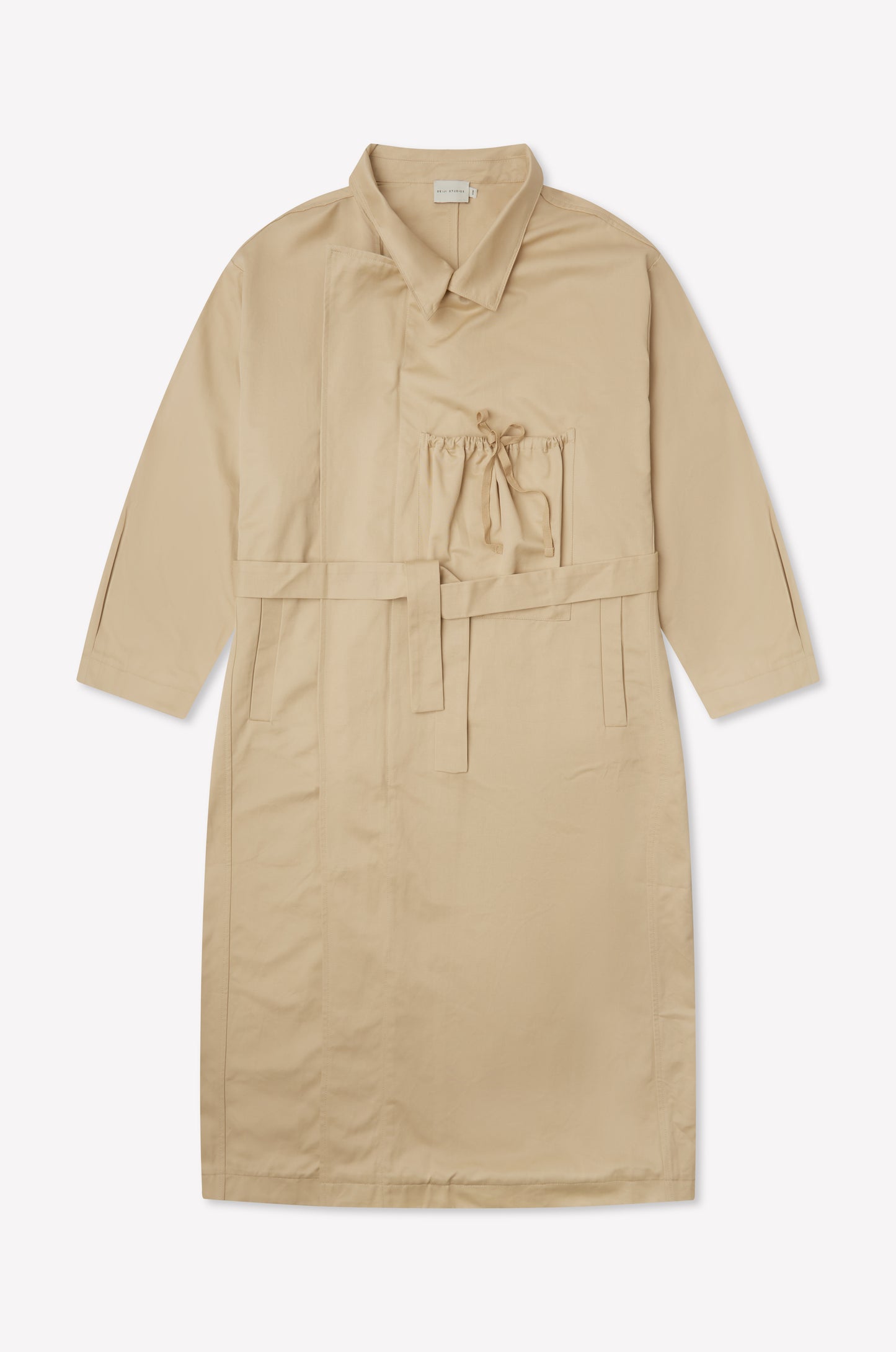 The Longline Jacket - Beige from Deiji Studios is a knee-length, beige coat with long sleeves, a belted waist, front pocket with drawstring, and collar, shown laid flat on a white background.
