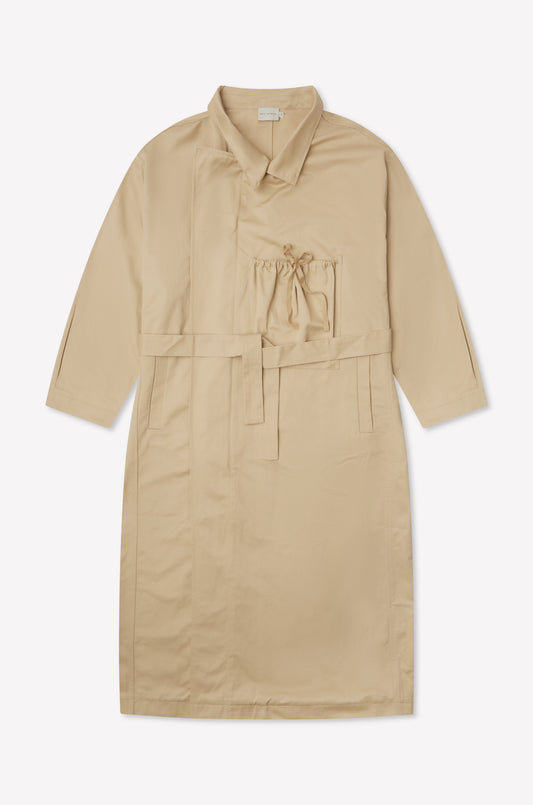 The Longline Jacket - Beige from Deiji Studios is a knee-length, beige coat with long sleeves, a belted waist, front pocket with drawstring, and collar, shown laid flat on a white background.