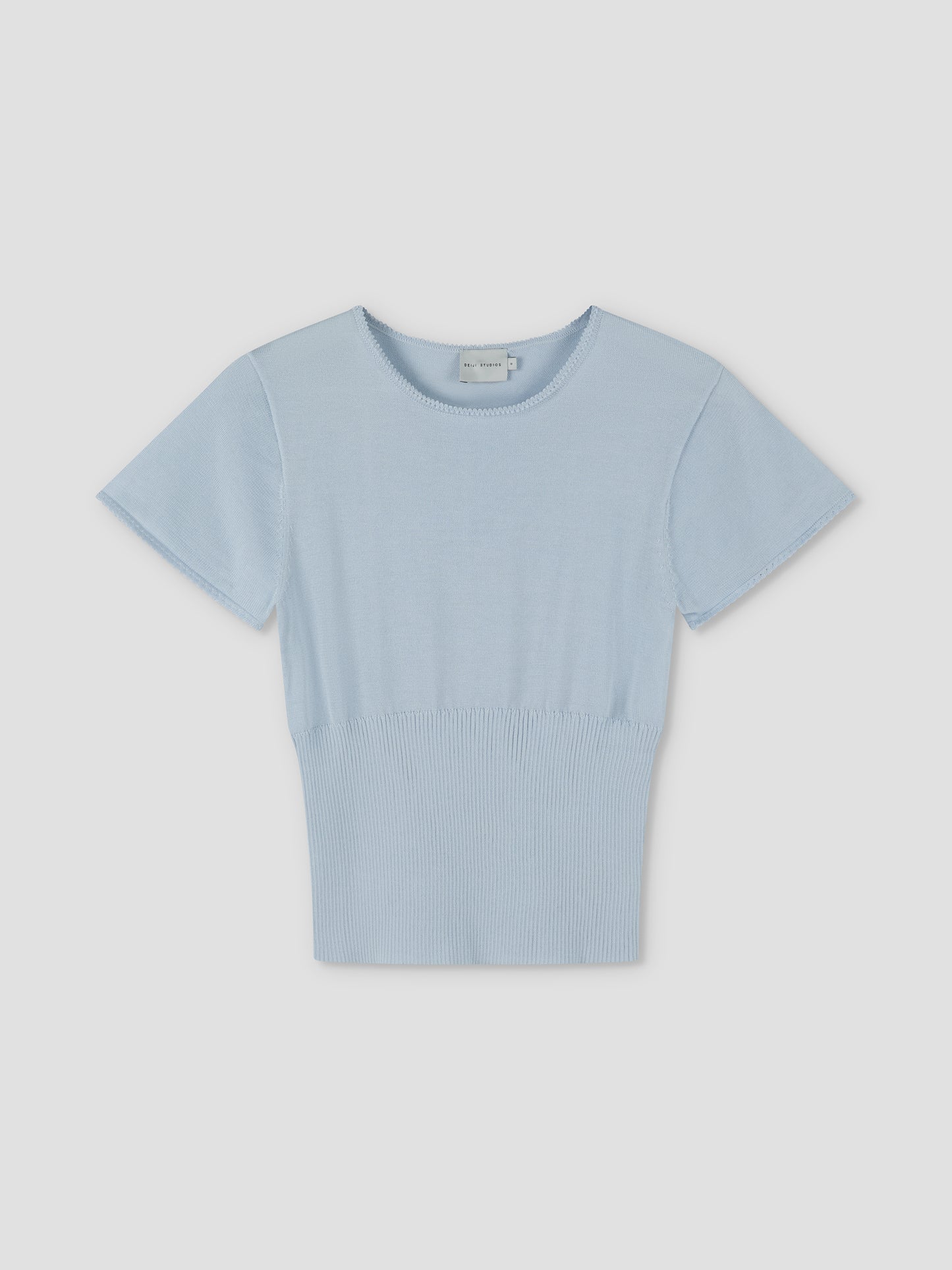 The Trim Knit Tee - Ice Blue features short sleeves, a round neckline, and a ribbed waistband. Displayed on a plain light background, it reflects Deiji Studios’ signature minimalist style in a fresh ice blue shade.