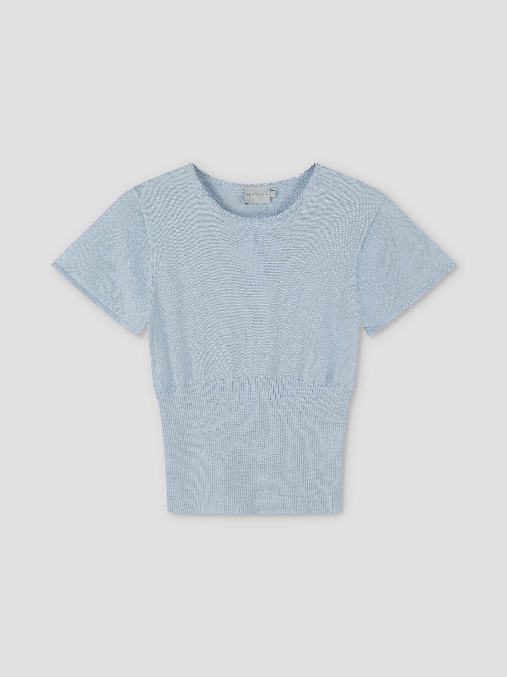 The Trim Knit Tee - Ice Blue features short sleeves, a round neckline, and a ribbed waistband. Displayed on a plain light background, it reflects Deiji Studios’ signature minimalist style in a fresh ice blue shade.