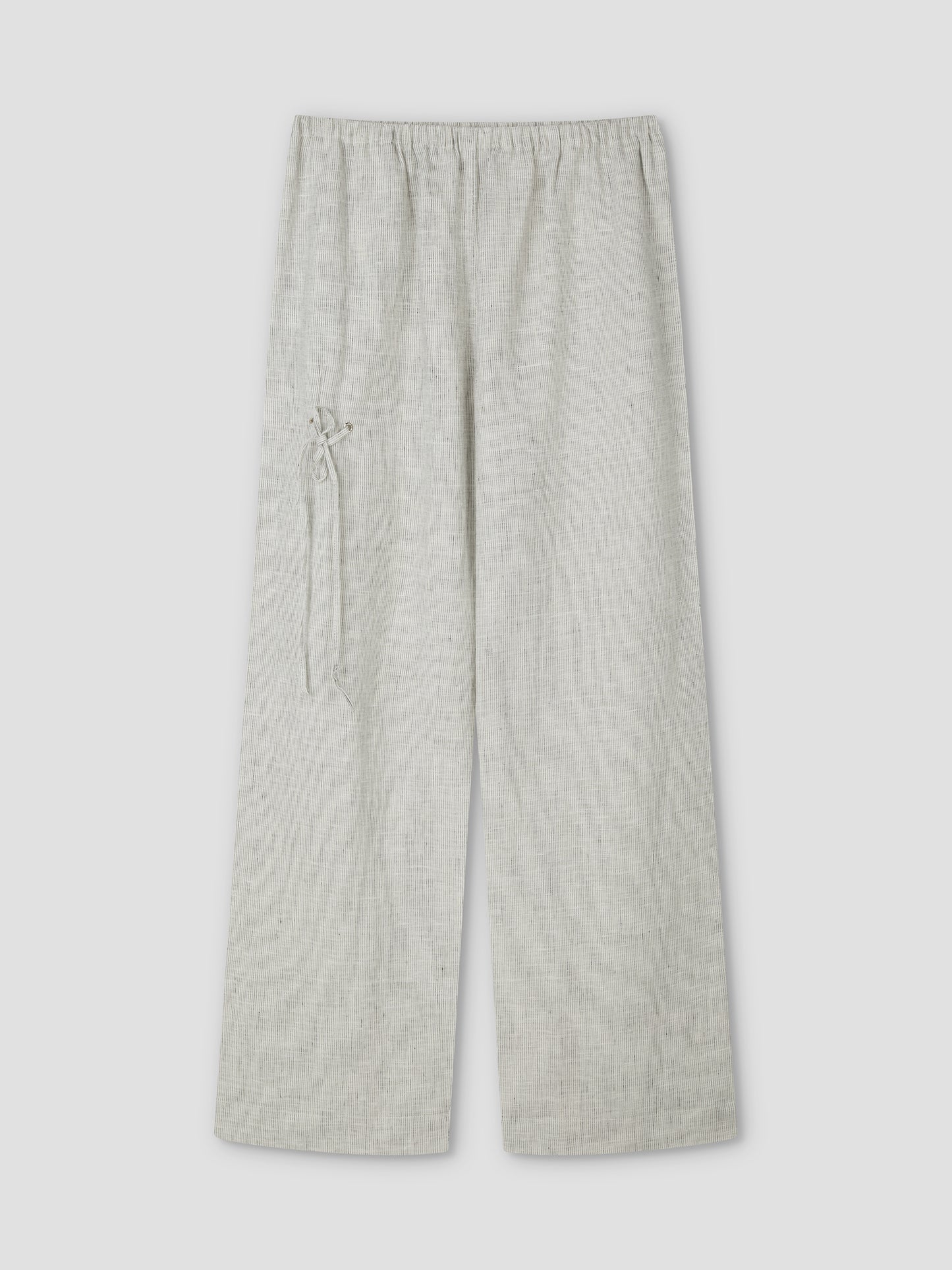 The Eyelet Pant - Fine Stripe by Deiji Studios features a light grey, wide-leg linen design with an elastic waistband, a decorative left-side tie, subtly textured fabric, and relaxed ankle length. Shown flat on a plain background.