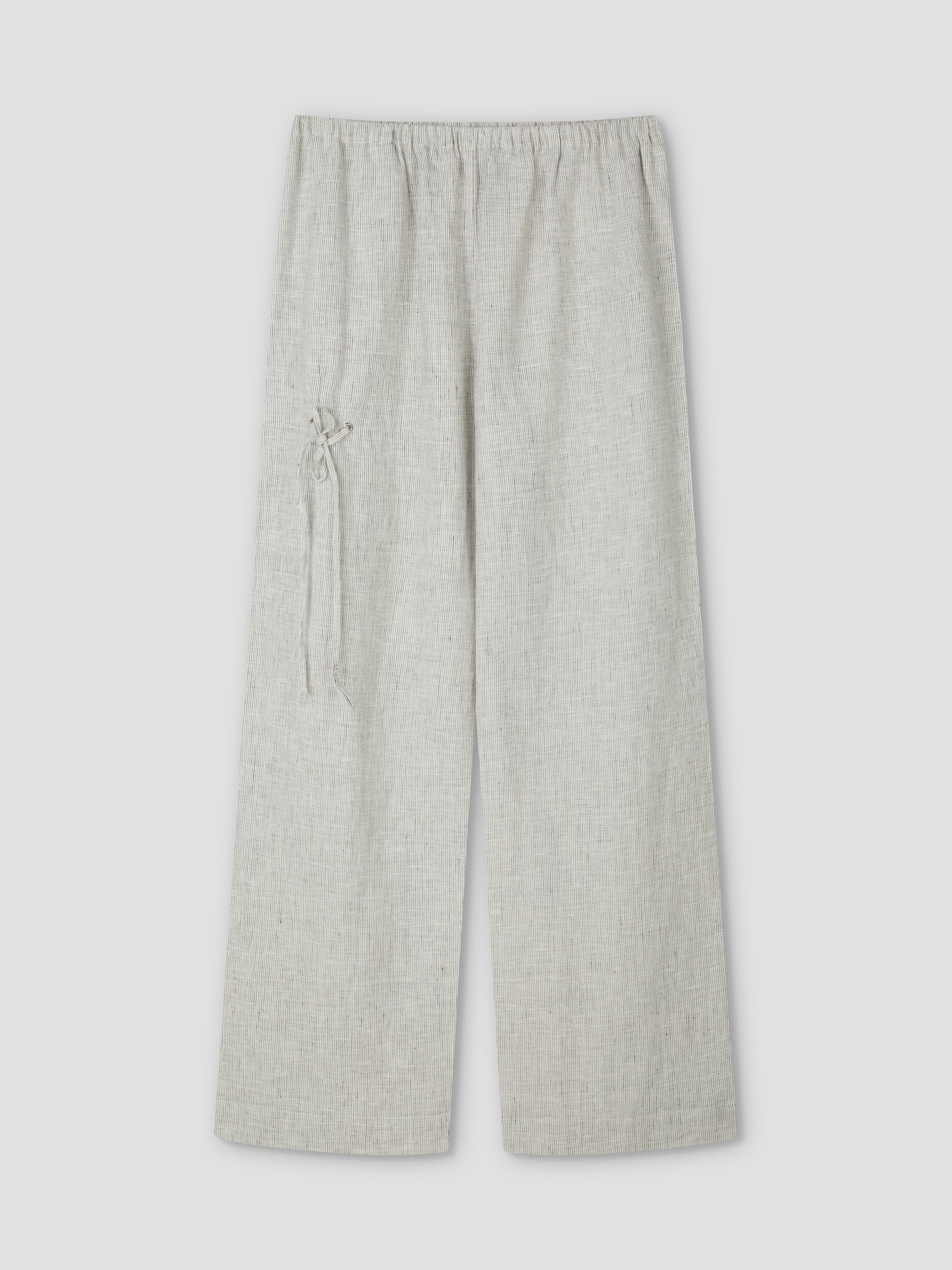 The Eyelet Pant - Fine Stripe by Deiji Studios features a light grey, wide-leg linen design with an elastic waistband, a decorative left-side tie, subtly textured fabric, and relaxed ankle length. Shown flat on a plain background.