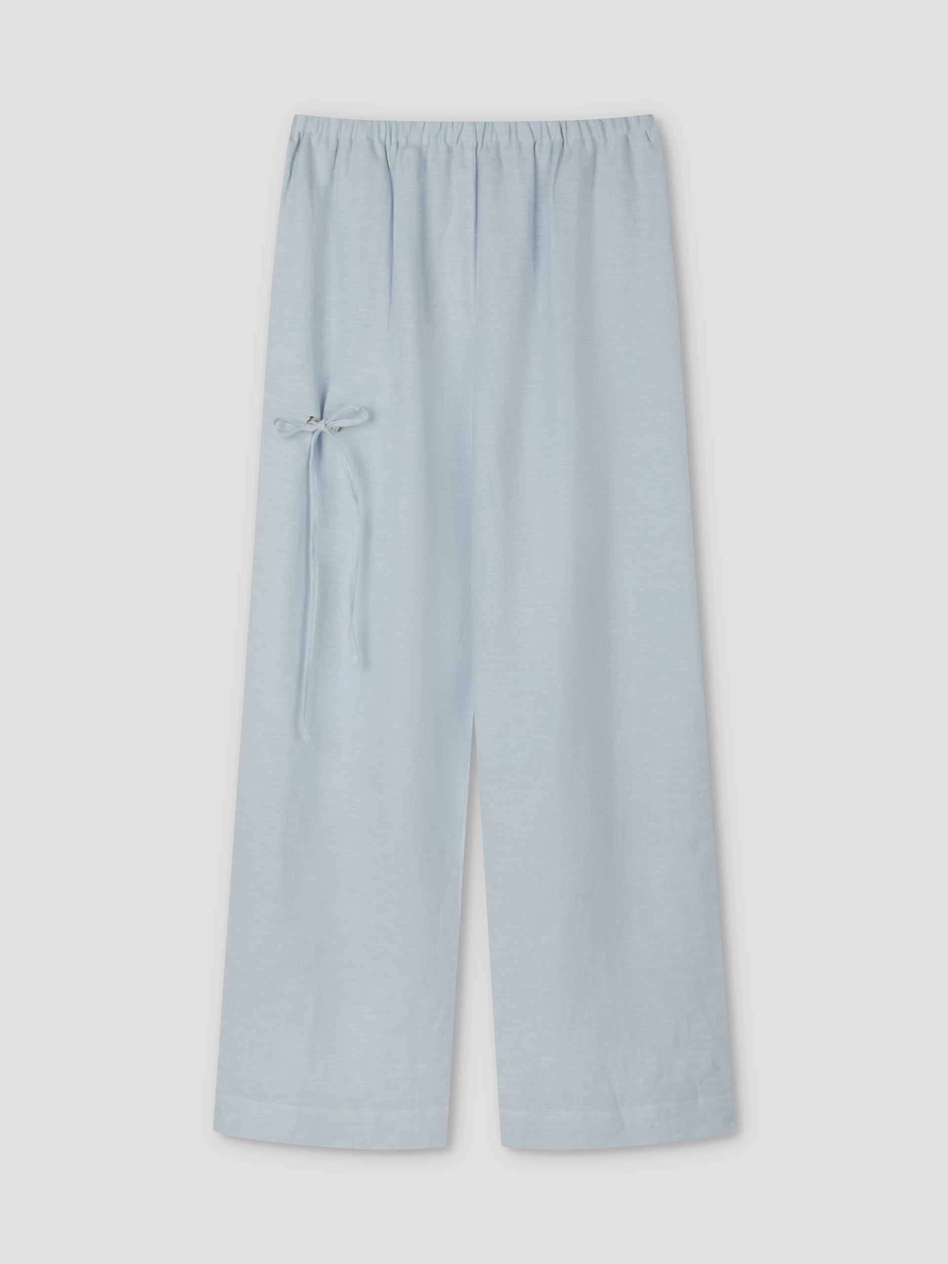 The Eyelet Pant - Soft Blue by Deiji Studios features wide-leg linen, a relaxed ankle length, an elastic waistband, and a small bow tie detail on the left side, displayed against a plain light background.