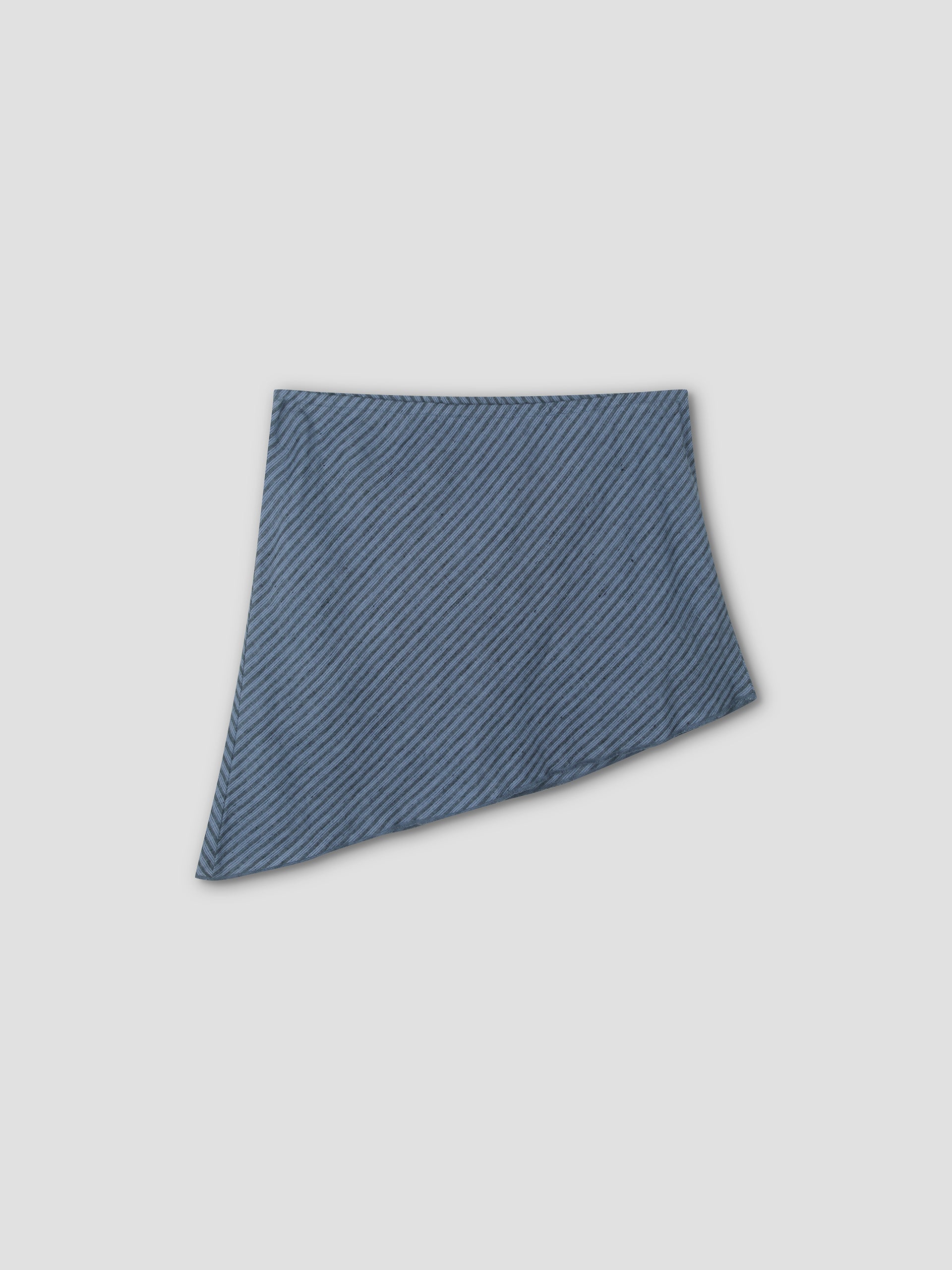 The Line Top - Azure Stripe features a modern, asymmetric design with diagonal stripes and a slanted hemline. Its simple style pairs well with lightweight skirts. Displayed on a plain light gray background.