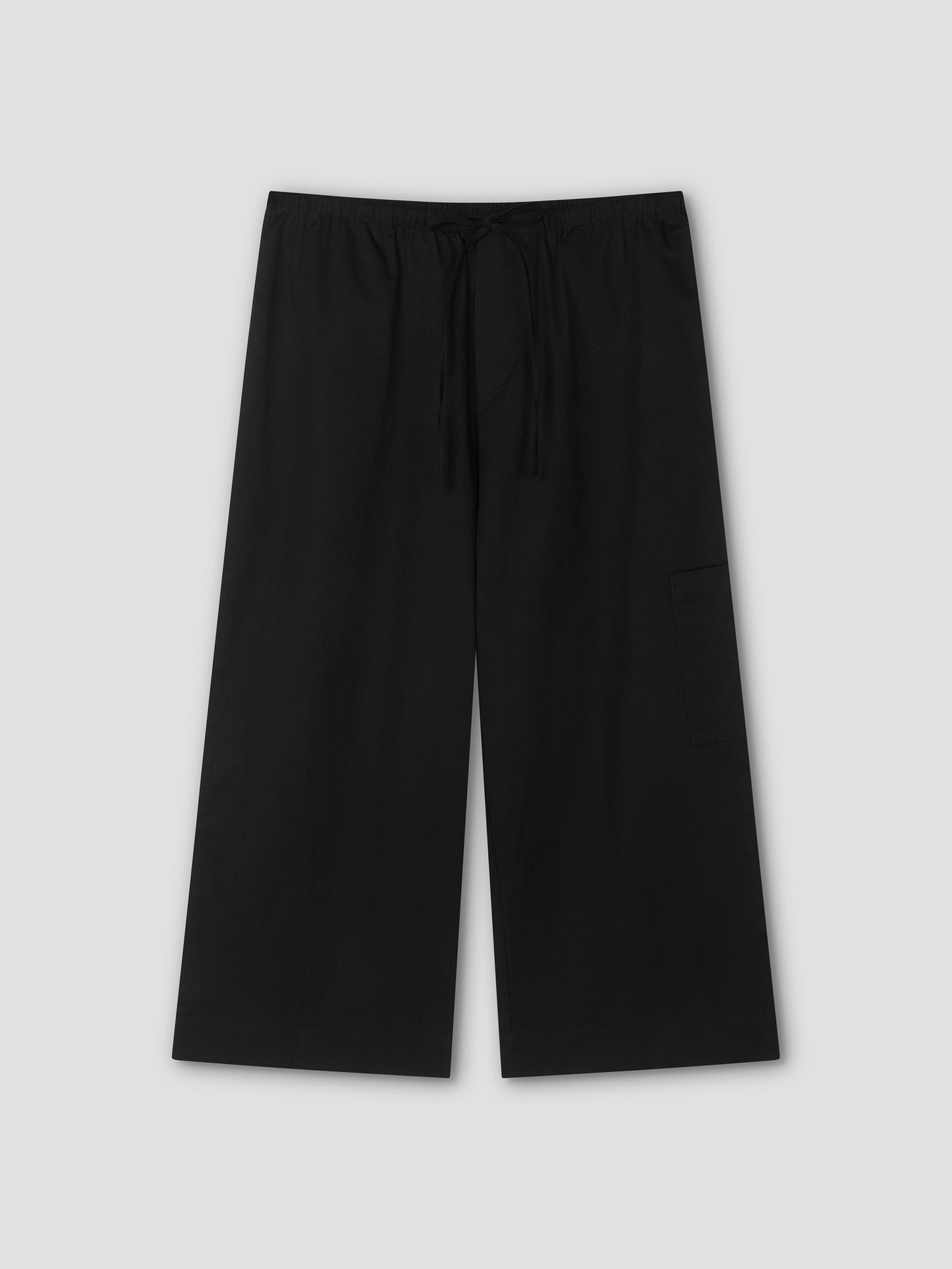 The Mid Pocket Short - Black by Deiji Studios features a relaxed, wide-leg fit with an elastic waistband, drawstring, and a visible right-side pocket. Displayed flat on a light gray background, these shorts evoke a comfortable 3/4 length style.