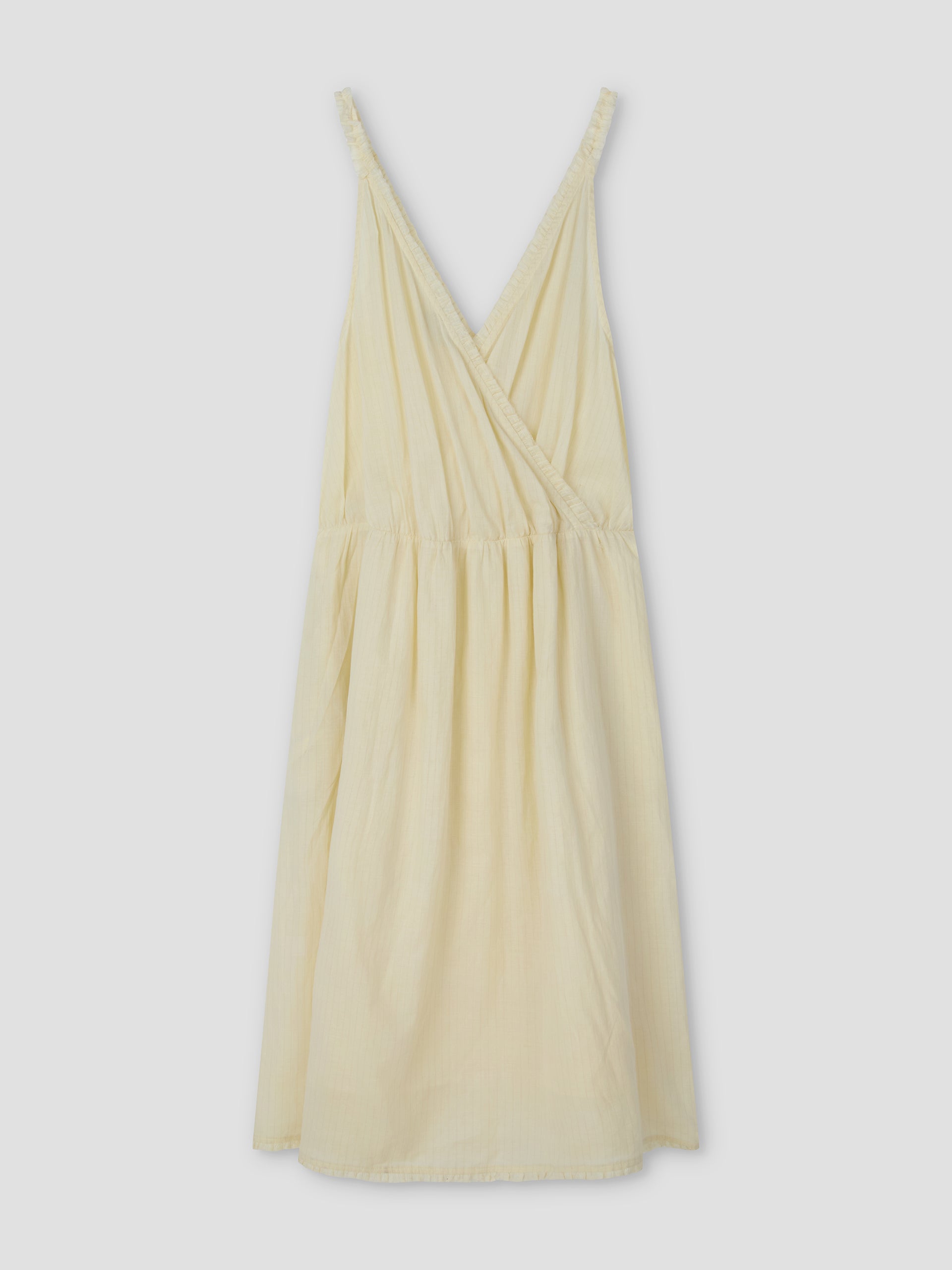 The Crossed Dress - Soft Yellow Stripe by Deiji Studios features a sleeveless, relaxed-fit design with a crossover v-neckline, gathered waist, and knee-length hem in lightweight striped fabric—perfect for effortless style.