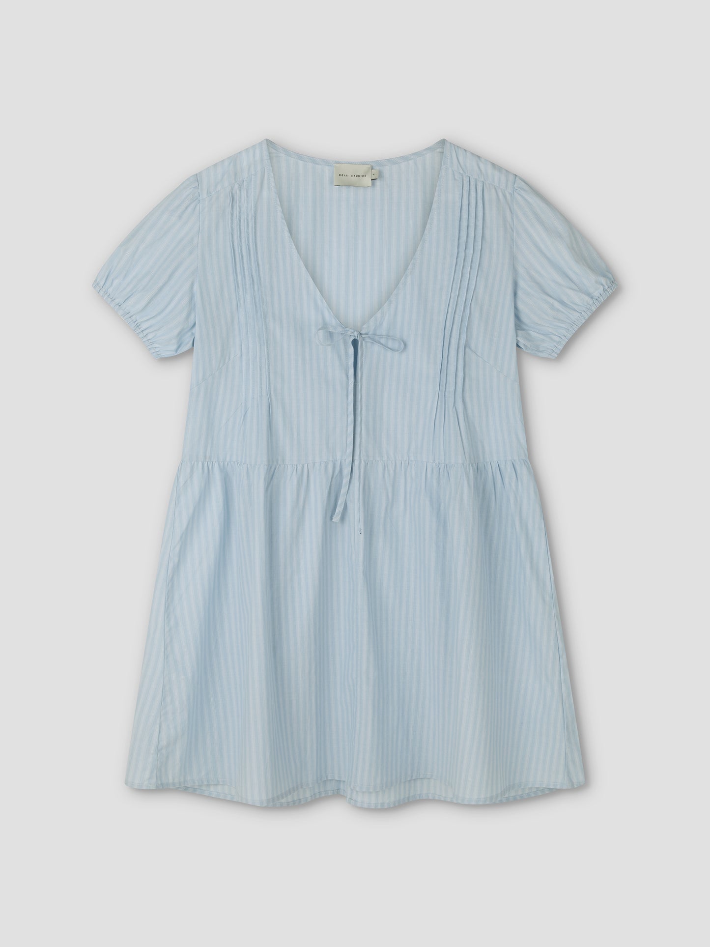 The V Pleat Dress - Lake Blue Stripe by Deiji Studios features a light blue hue with thin white vertical stripes, short sleeves, a V-neckline with tie detail, and slight bodice pleating for a relaxed, comfortable everyday fit.