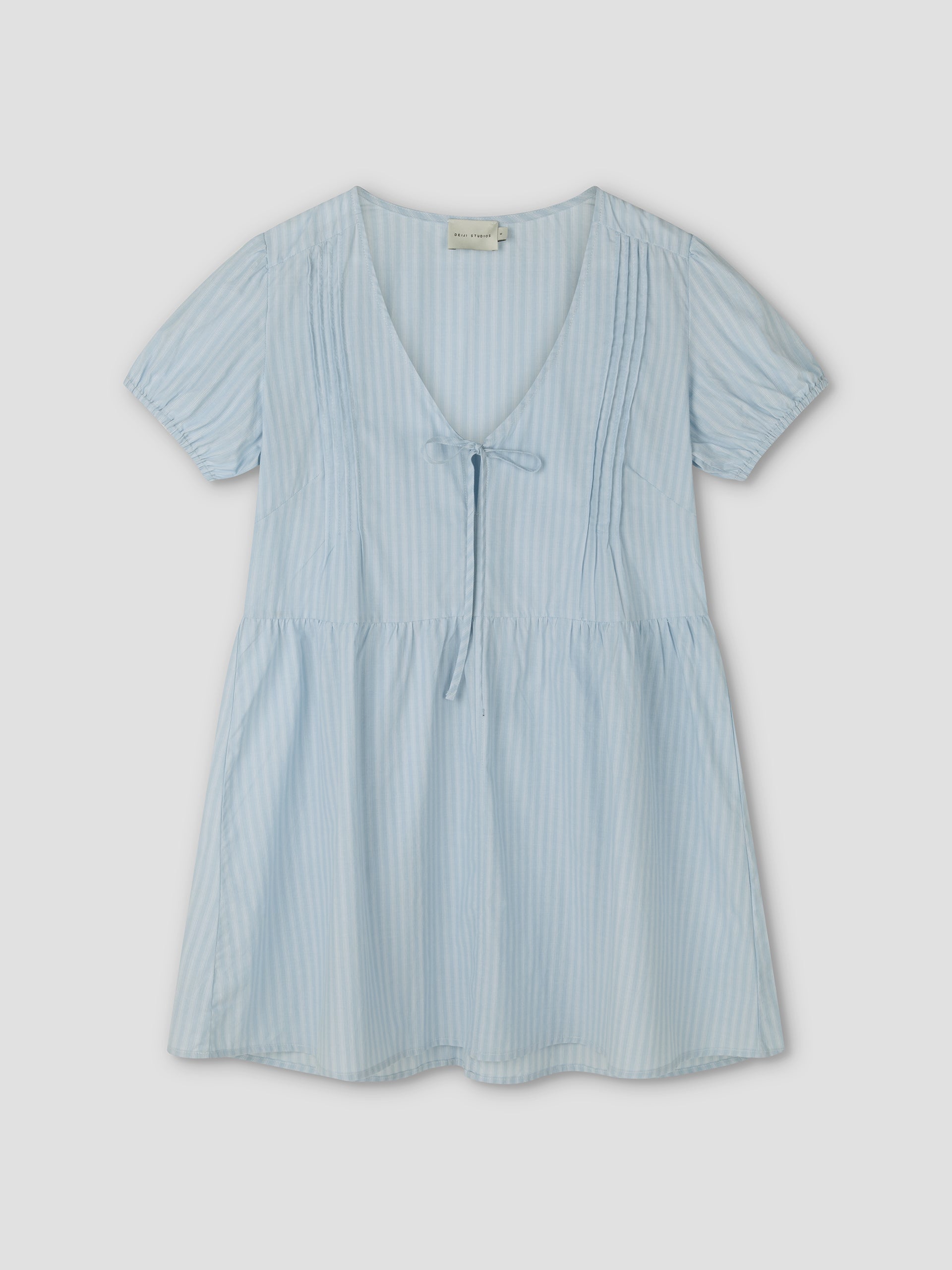 The V Pleat Dress - Lake Blue Stripe by Deiji Studios features a light blue hue with thin white vertical stripes, short sleeves, a V-neckline with tie detail, and slight bodice pleating for a relaxed, comfortable everyday fit.