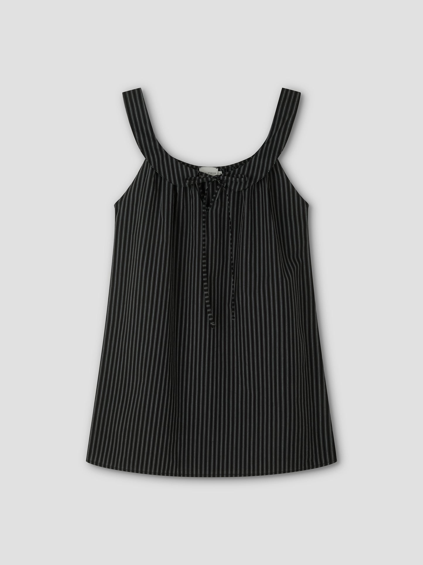 The Rounded Neck Dress - Mono stripe features a black sleeveless design with thin white vertical pinstripes, wide shoulder straps, a front tie detail, and a rounded neckline. It is displayed against a plain light gray background.