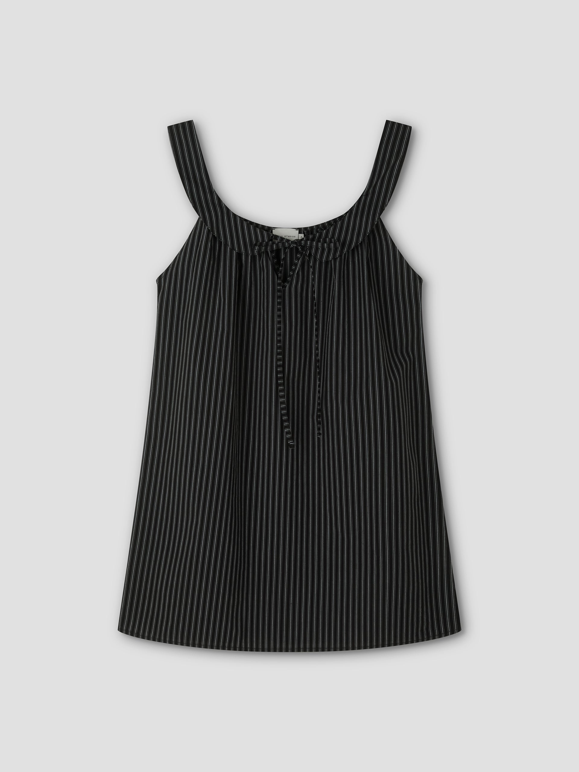 The Rounded Neck Dress - Mono stripe features a black sleeveless design with thin white vertical pinstripes, wide shoulder straps, a front tie detail, and a rounded neckline. It is displayed against a plain light gray background.