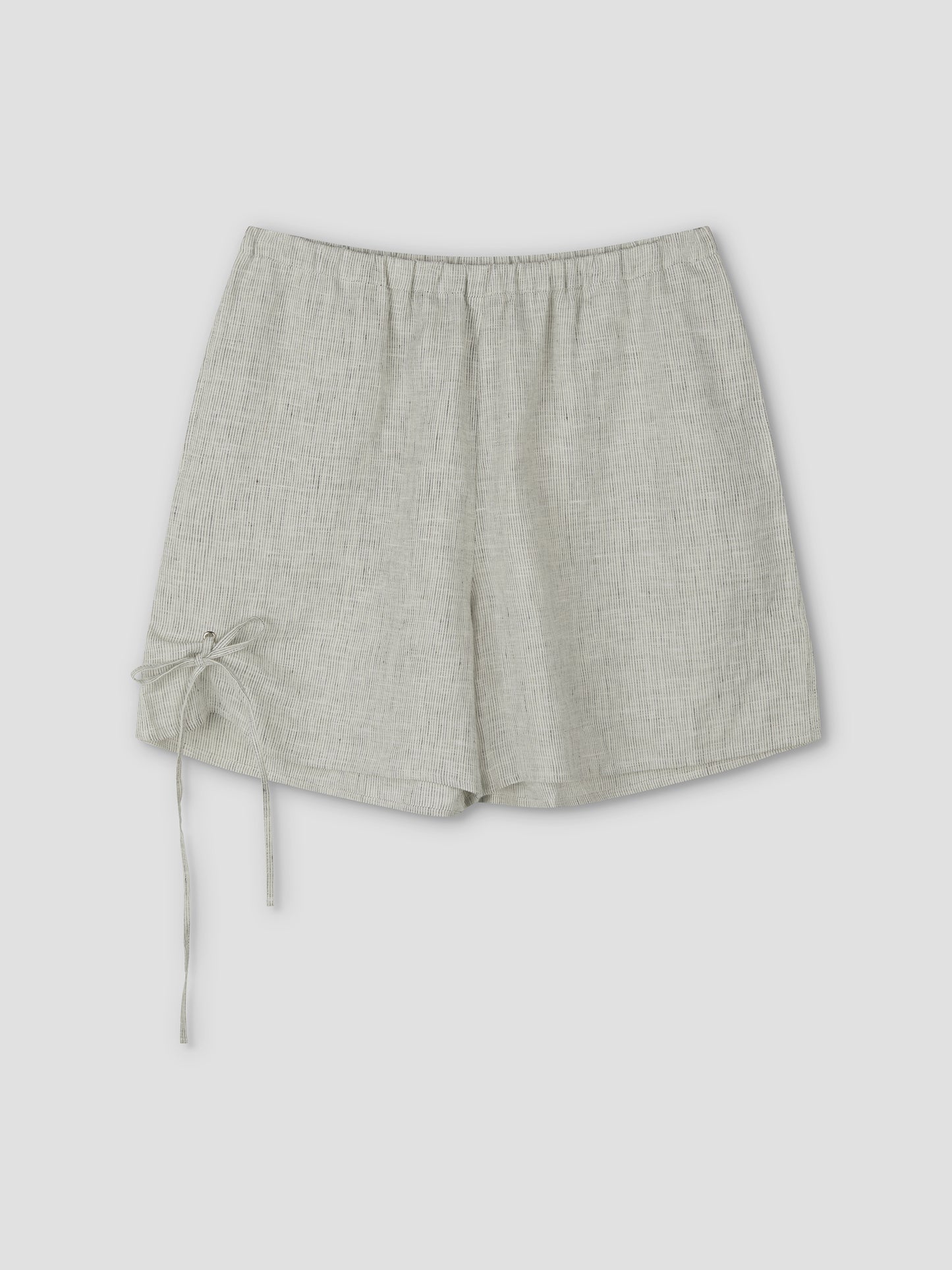 The Eyelet Short - Fine Stripe features a light gray linen, elastic waistband, and a decorative left tie, shown on a plain light background. Inspired by Deiji Studios' signature relaxed style.