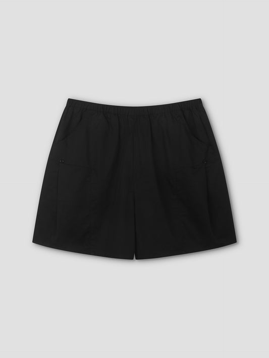 The Pleat Short - Black features a relaxed mid-rise fit, elastic waistband, and two front pockets, shown flat on a light grey background—a minimalist staple by Deiji Studios.