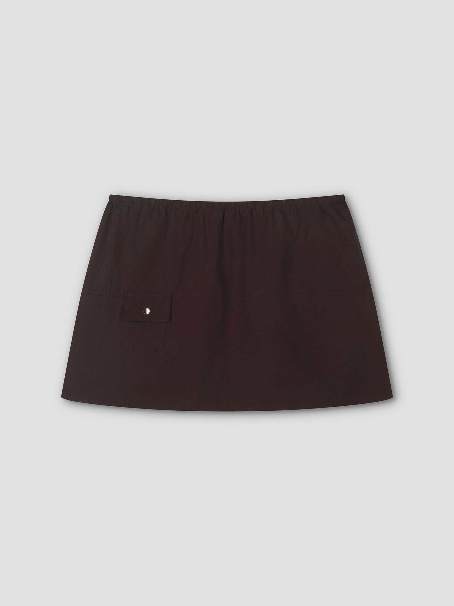 The Pocket Skirt - Sepia features an elastic waistband and a small buttoned flap pocket on the left, true to Deiji Studios style. This chic black mini skirt is displayed against a plain light gray background, perfect for any occasion.