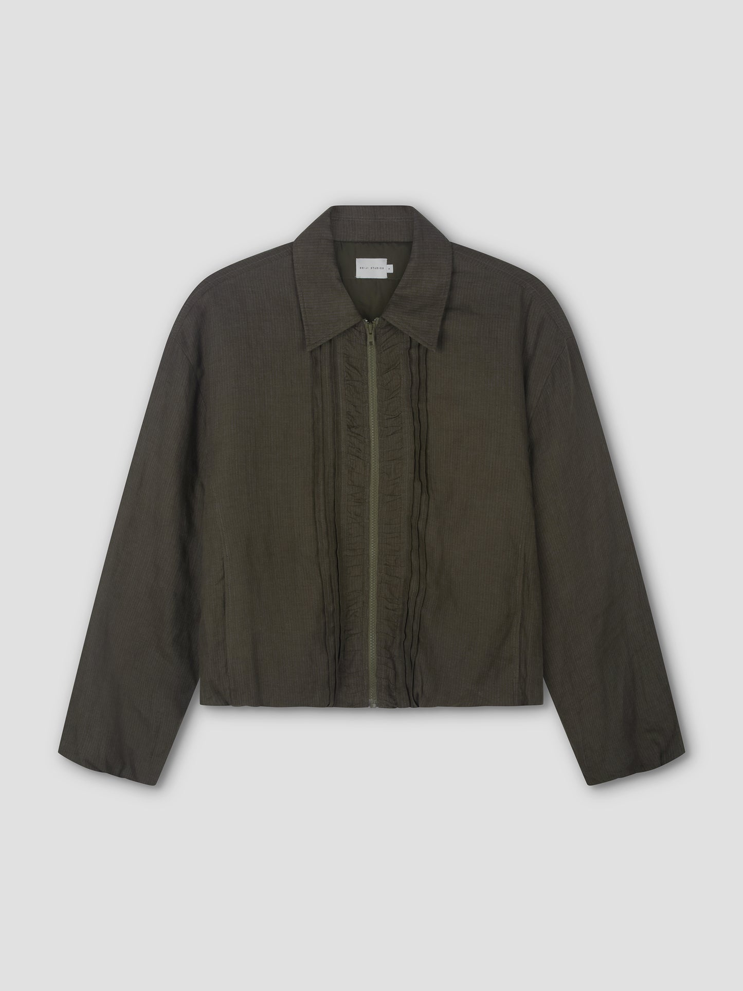 The Pintuck Jacket - Khaki Stripe by Deiji Studios is a dark olive green, long-sleeved bomber with a classic collar, front zip, subtle vertical ruffle details beside the zipper, and a straight hem. Shown laid flat on a light background.