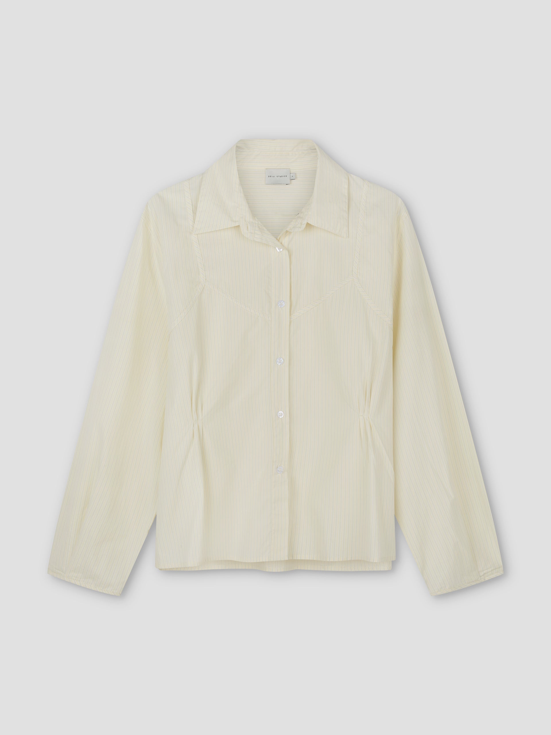 The Cami Overshirt - Citrus Stripe by Deiji Studios is a lightweight, long-sleeve button-up in light yellow with vertical stripes and gentle waist gathering, shown flat against a plain background.