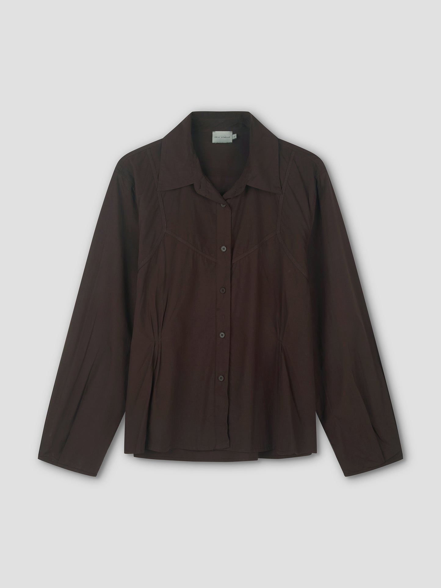 The Cami Overshirt - Sepia is a long-sleeved, dark brown button-up shirt with a pointed collar and subtle seam details, perfect for relaxed layering or wearing over a cami, shown on a plain light background.