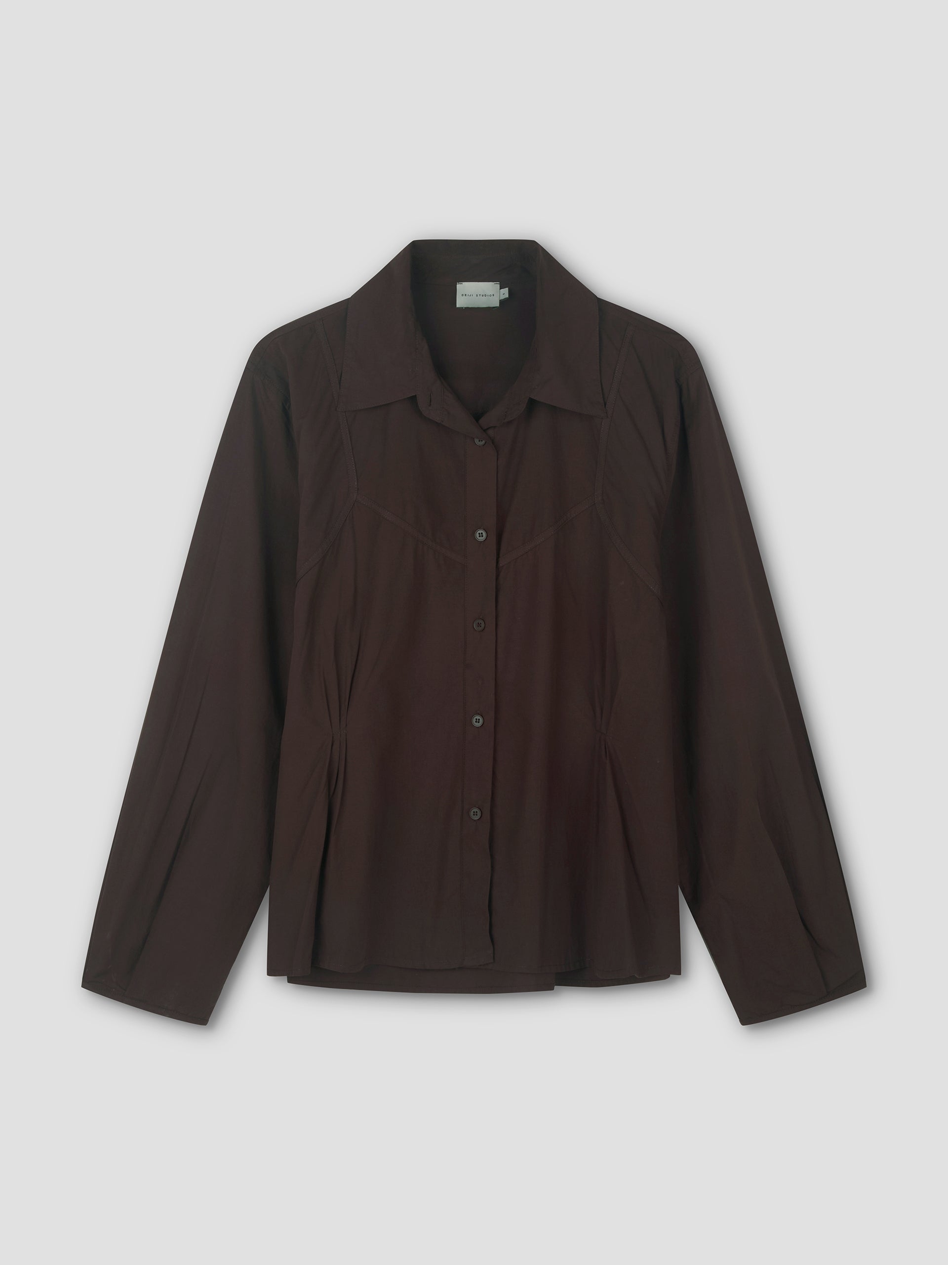 The Cami Overshirt - Sepia is a long-sleeved, dark brown button-up shirt with a pointed collar and subtle seam details, perfect for relaxed layering or wearing over a cami, shown on a plain light background.
