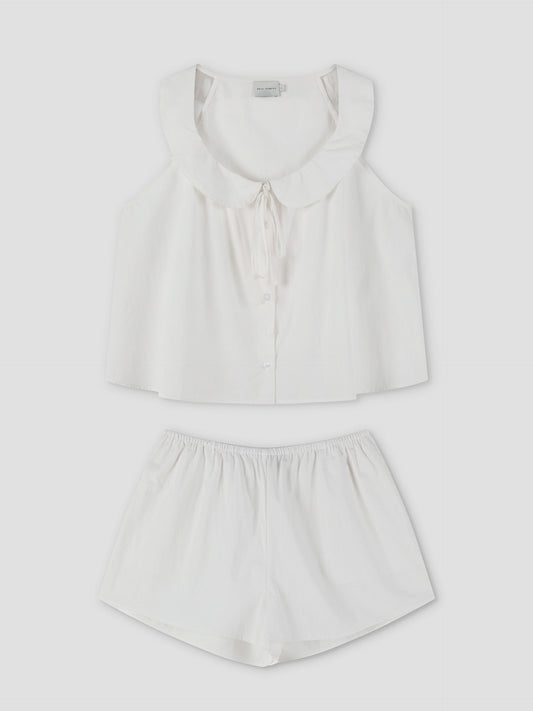 The Round Collar Set - White Texture features a white sleeveless pajama top with a ruffled collar and tie detail, button-up front, and matching loose-fitting shorts, displayed flat on a white background. Inspired by Deiji Studios.