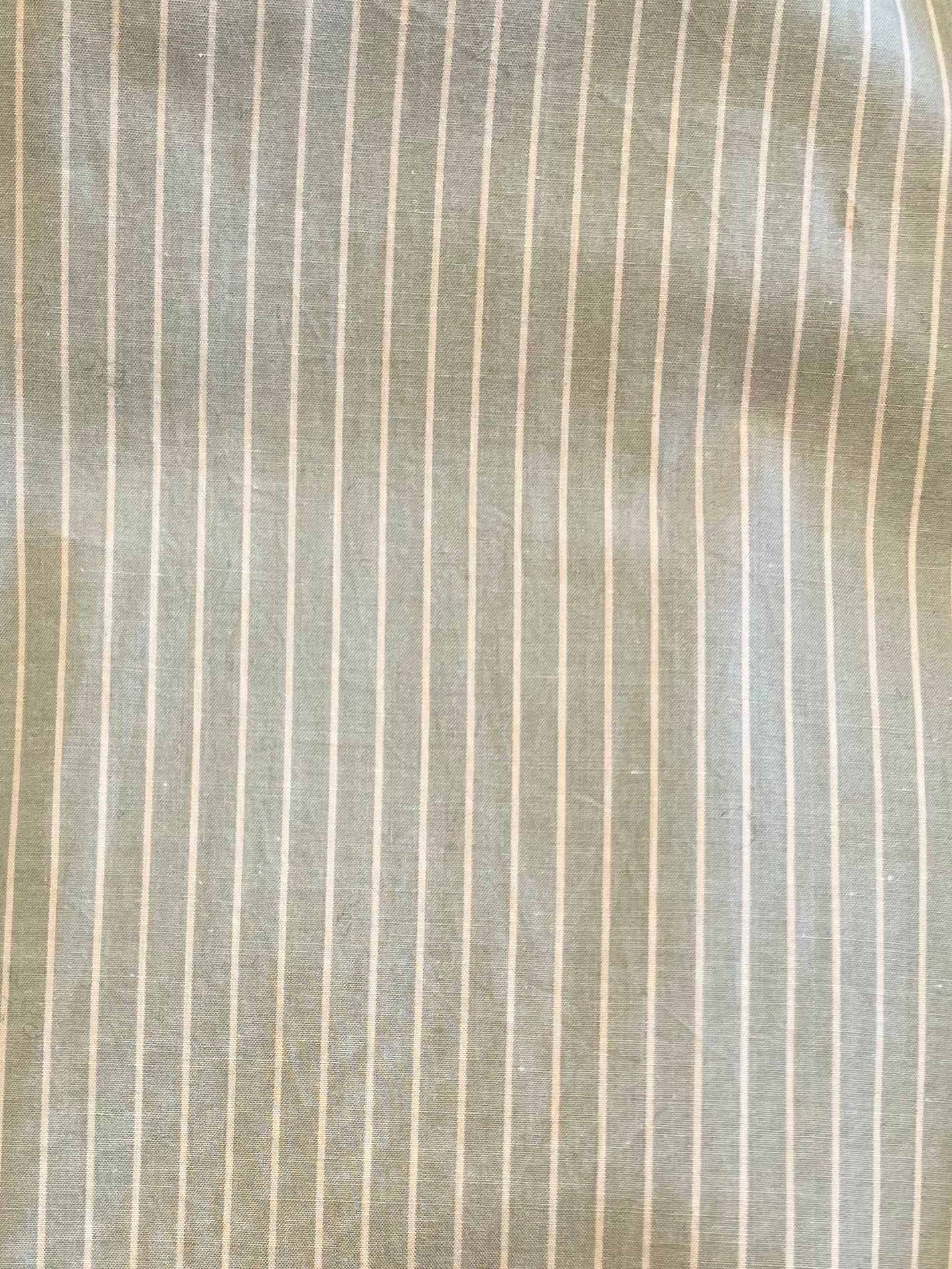 A close-up of the Long Lounger - Pistachio Stripe shows light gray organic cotton with thin white pinstripes, slight wrinkles, and a textured look—ideal for relaxing in comfort.