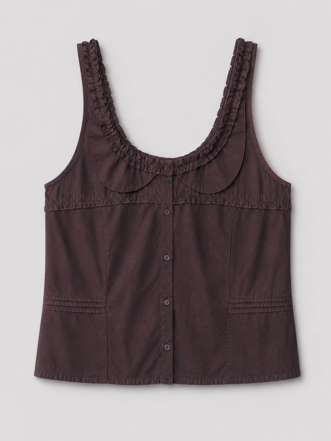 The Frills Top - Toast is a sleeveless, dark brown cotton poplin blouse with a scoop neckline, ruffled trim, decorative stitching, rounded collar, frill accents, and two front pockets. Shown on a plain light gray background.
