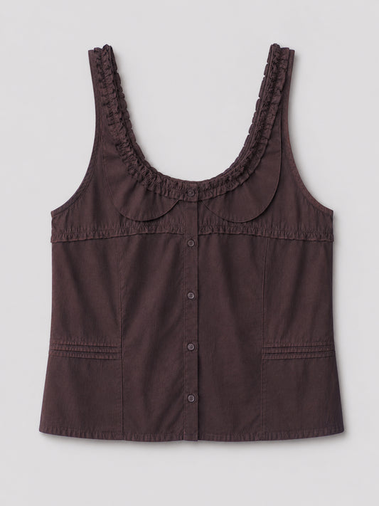 The Frills Top - Toast is a sleeveless, dark brown cotton poplin blouse with a scoop neckline, ruffled trim, decorative stitching, rounded collar, frill accents, and two front pockets. Shown on a plain light gray background.