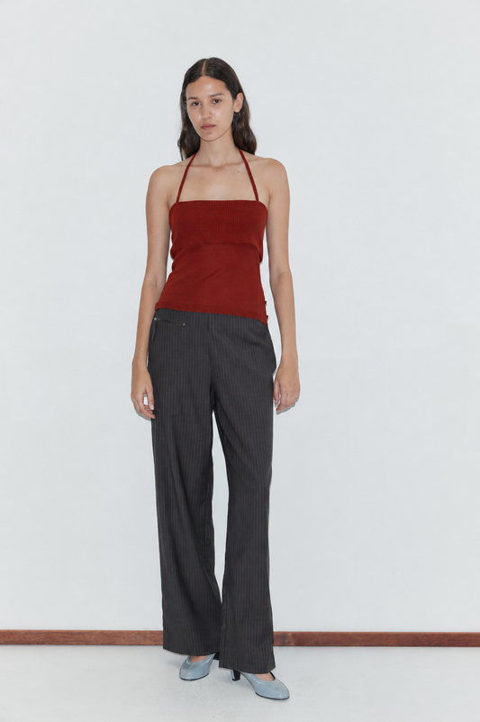 A woman stands against a plain white background, wearing the Half Top - Red by Deiji Studios, paired with dark pinstripe pants and light blue heels.