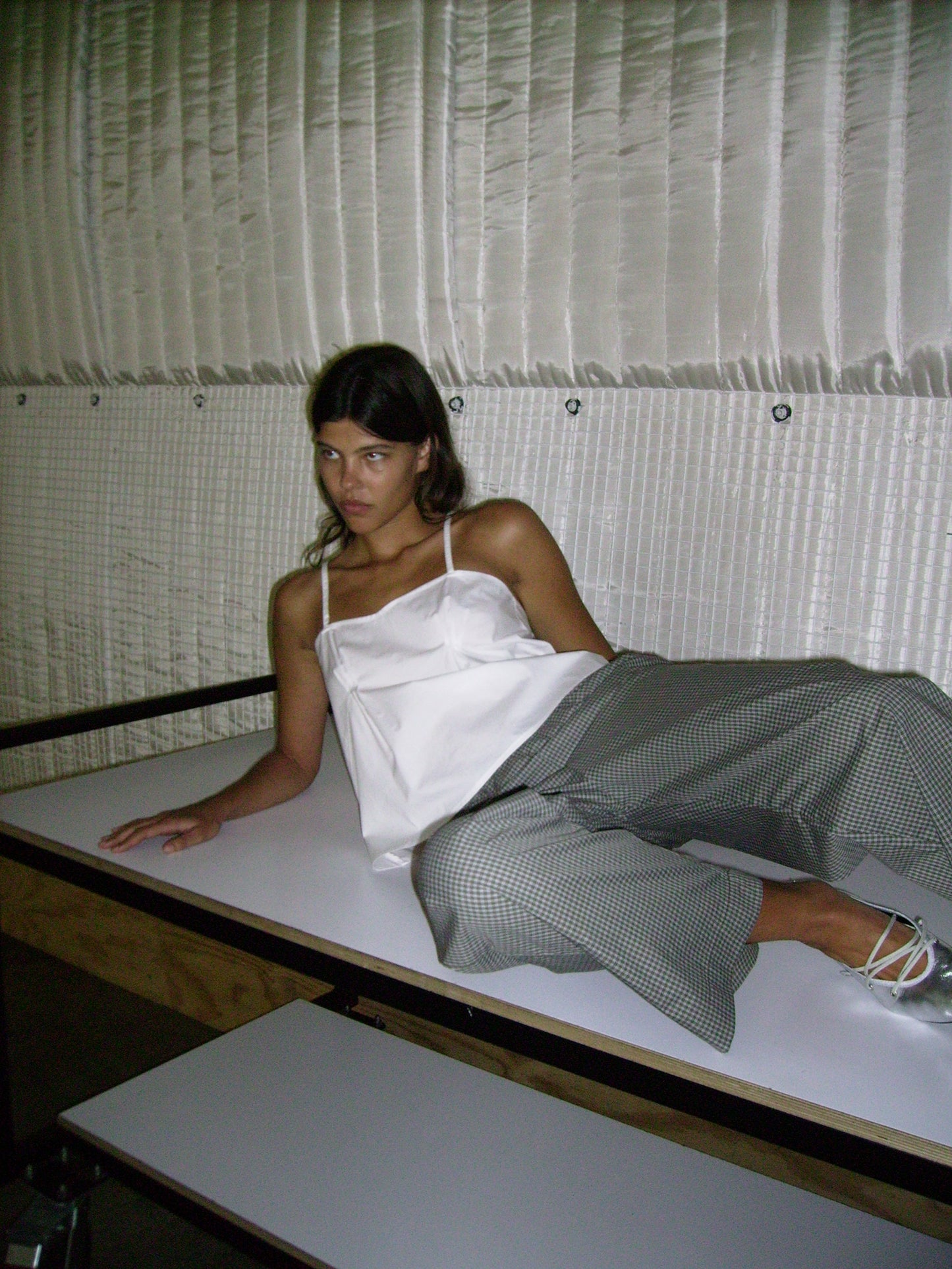 Female model laying on table wearing Pleat Top - White by Deiji Studios against plain background