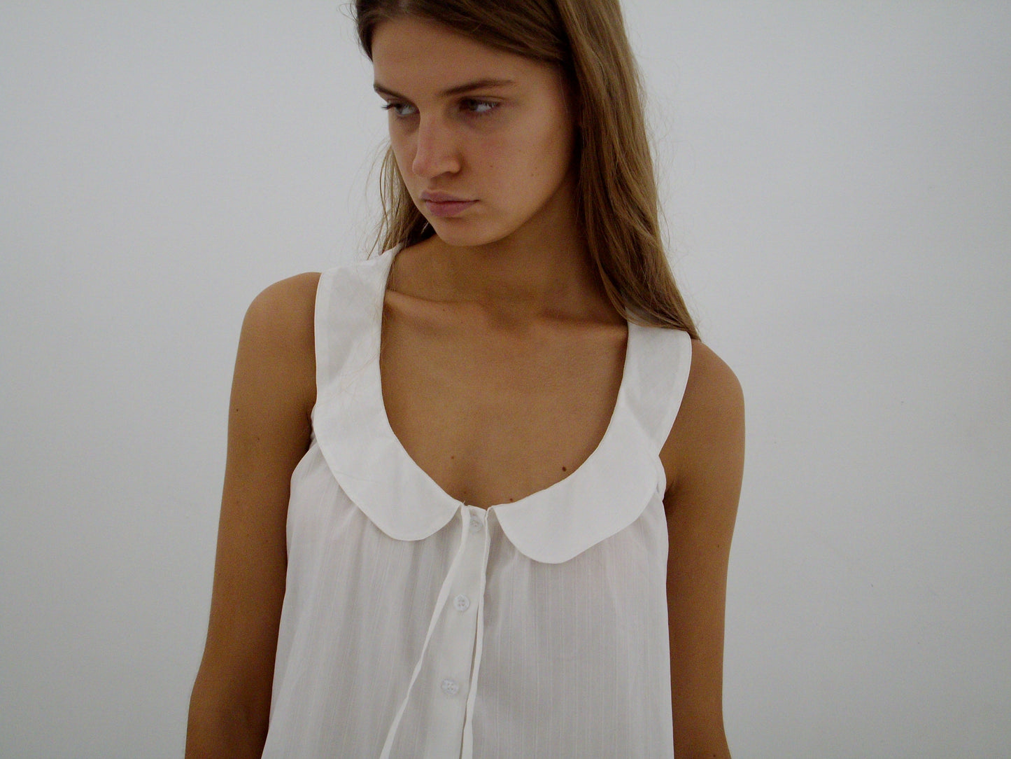 A young woman with long brown hair wears the Round Collar Top - White Texture by Deiji Studios, looking slightly down and to the side against a plain white background.