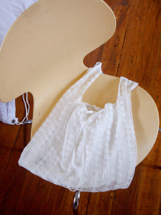 A Deiji Studios Thread Dust Bag in off white is draped over the seat of a light-colored, modern curved chair on a wooden floor.