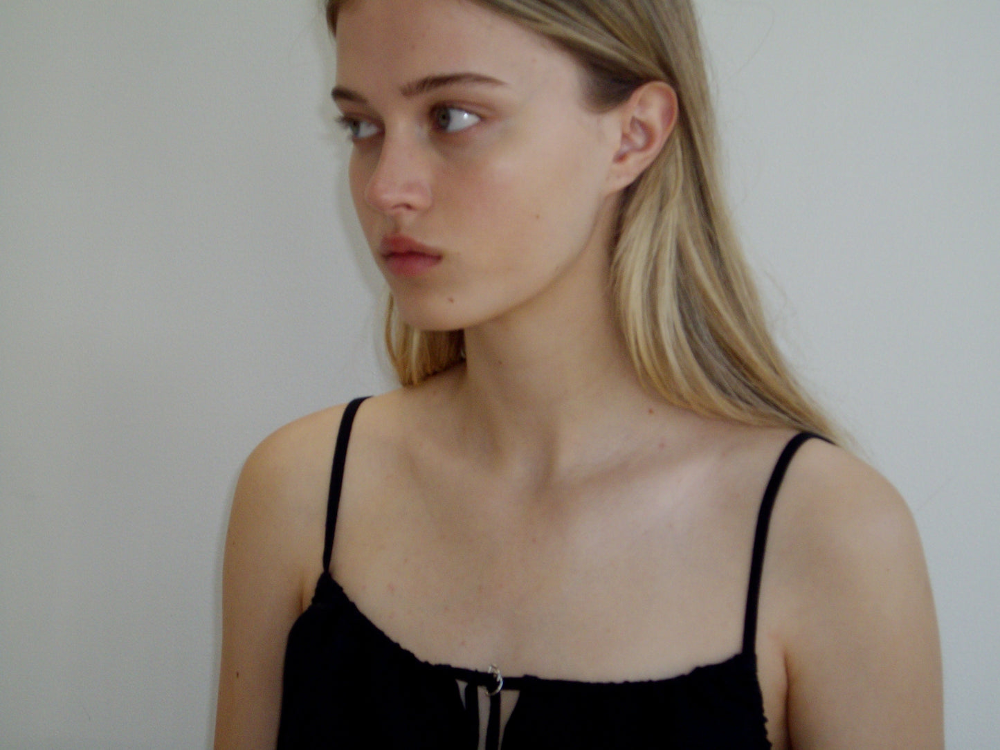 A young woman with long blonde hair, wearing the Lettuce Mini Dress in black, looks to her left against a plain light background with a neutral expression.
