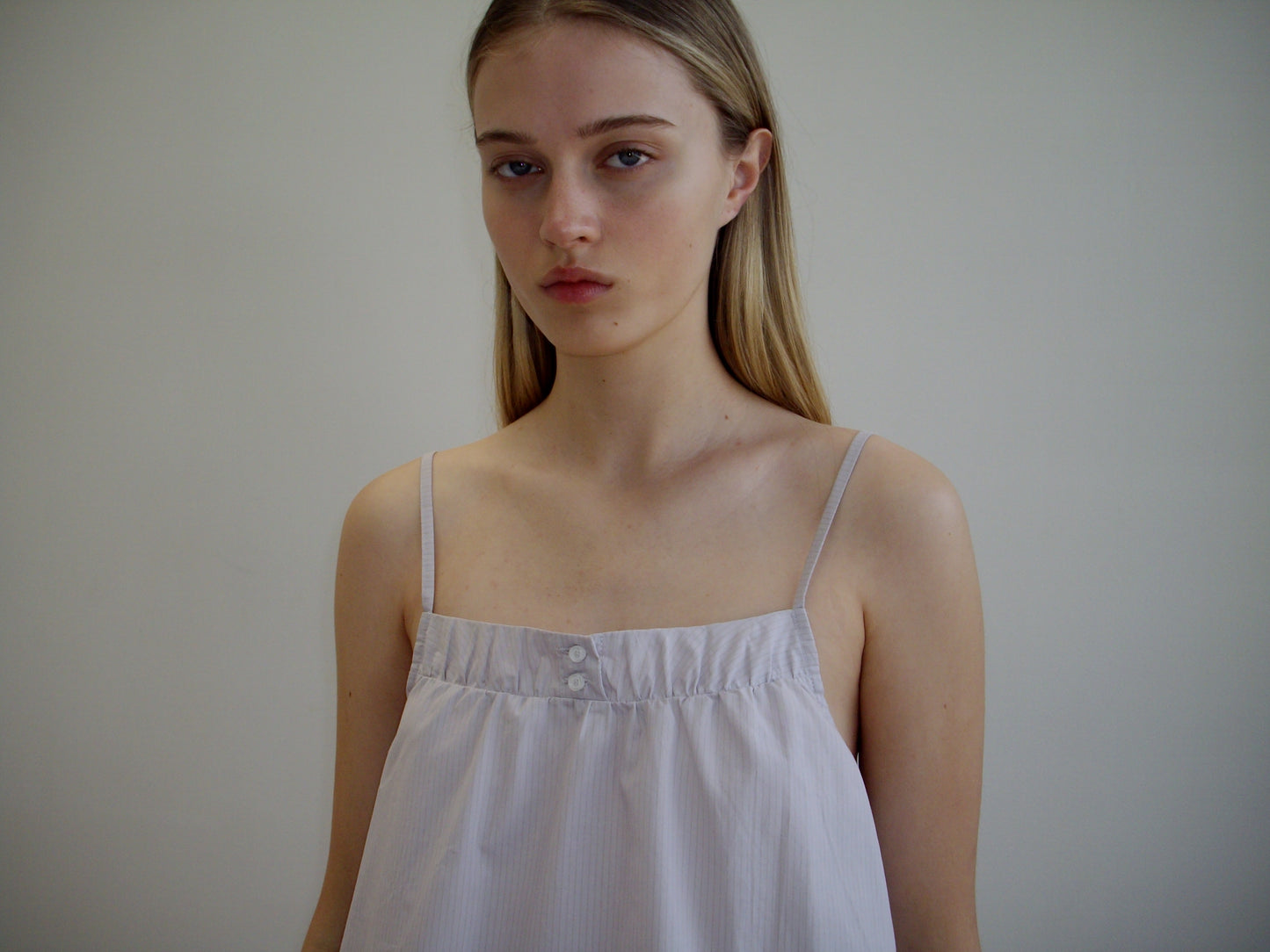 A young woman with long, straight blonde hair wears the Yoke Set - Lilac Stripe by Deiji Studios, featuring a loose, light-colored organic cotton poplin babydoll top. She faces forward with a neutral expression against a plain background.