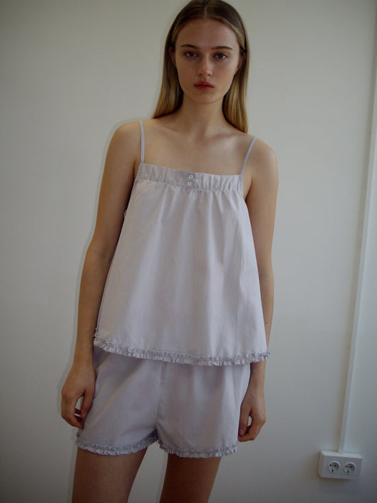 A woman with long, straight blonde hair stands against a plain light wall, wearing the Yoke Set - Lilac Stripe by Deiji Studios. She has a neutral expression and relaxed posture.