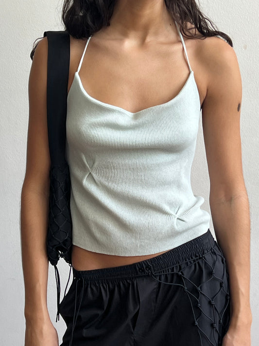 A woman wearing a Fine Knot Tank in ice blue and black drawstring pants with a black woven shoulder bag stands against a plain white background.