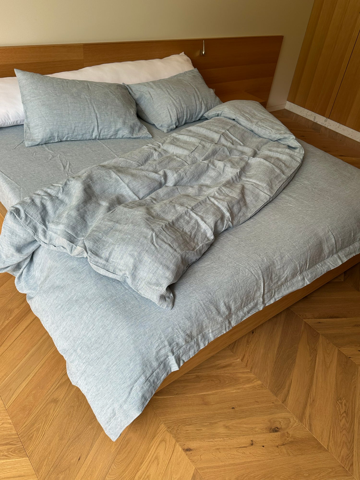 A neatly made bed with the Blue Stripe duvet cover and two pillows sits against a wooden headboard on a chevron-patterned floor, creating a minimalist, tidy room with hypo-allergenic accents.