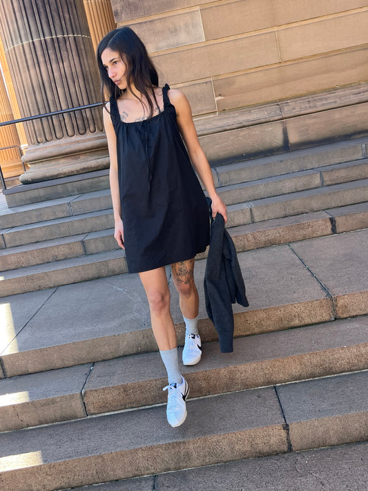 Female model wearing the bow dress - black by Deiji Studios against gallery entrance stairs